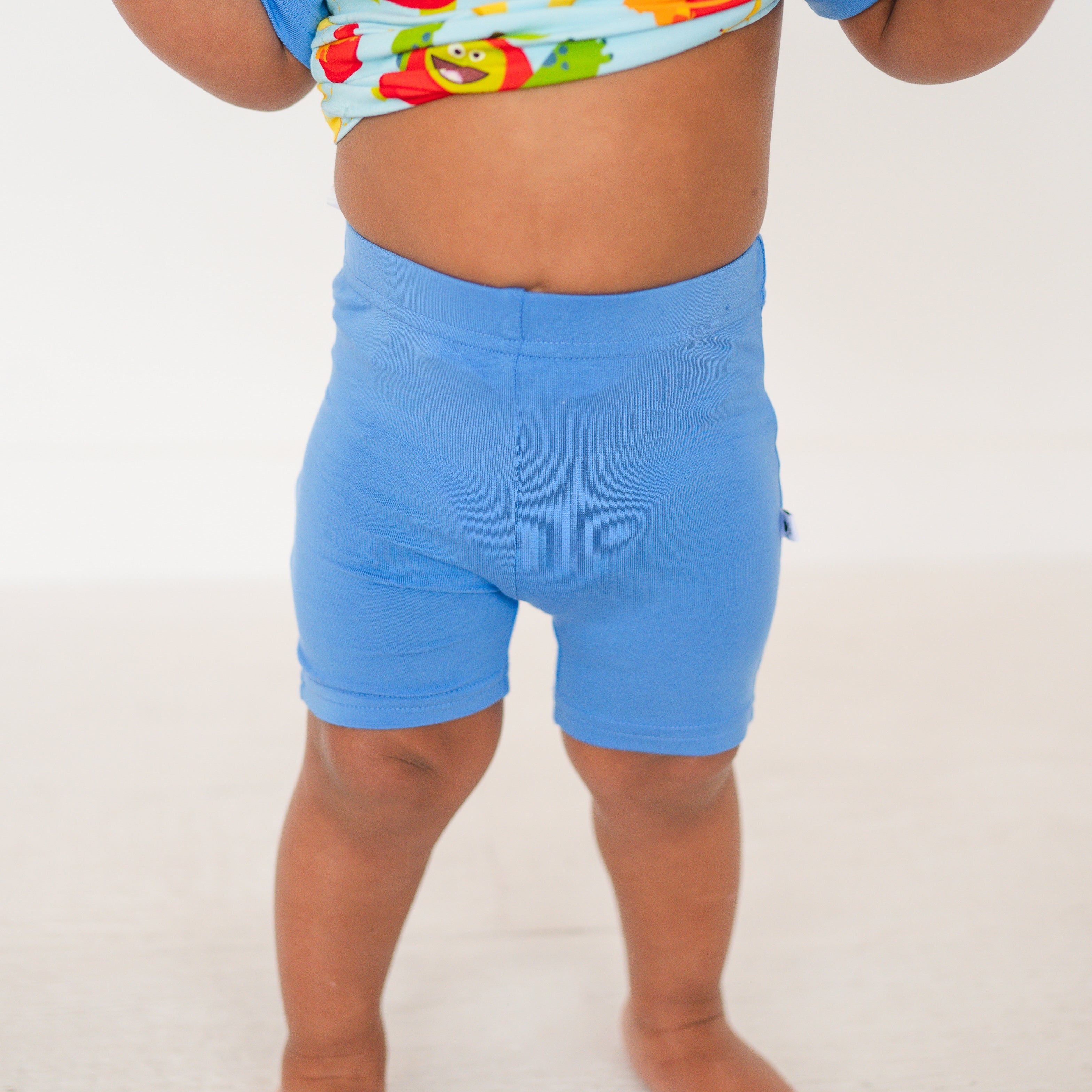 A child wears blue biker shorts and a colorful monster-patterned top.
