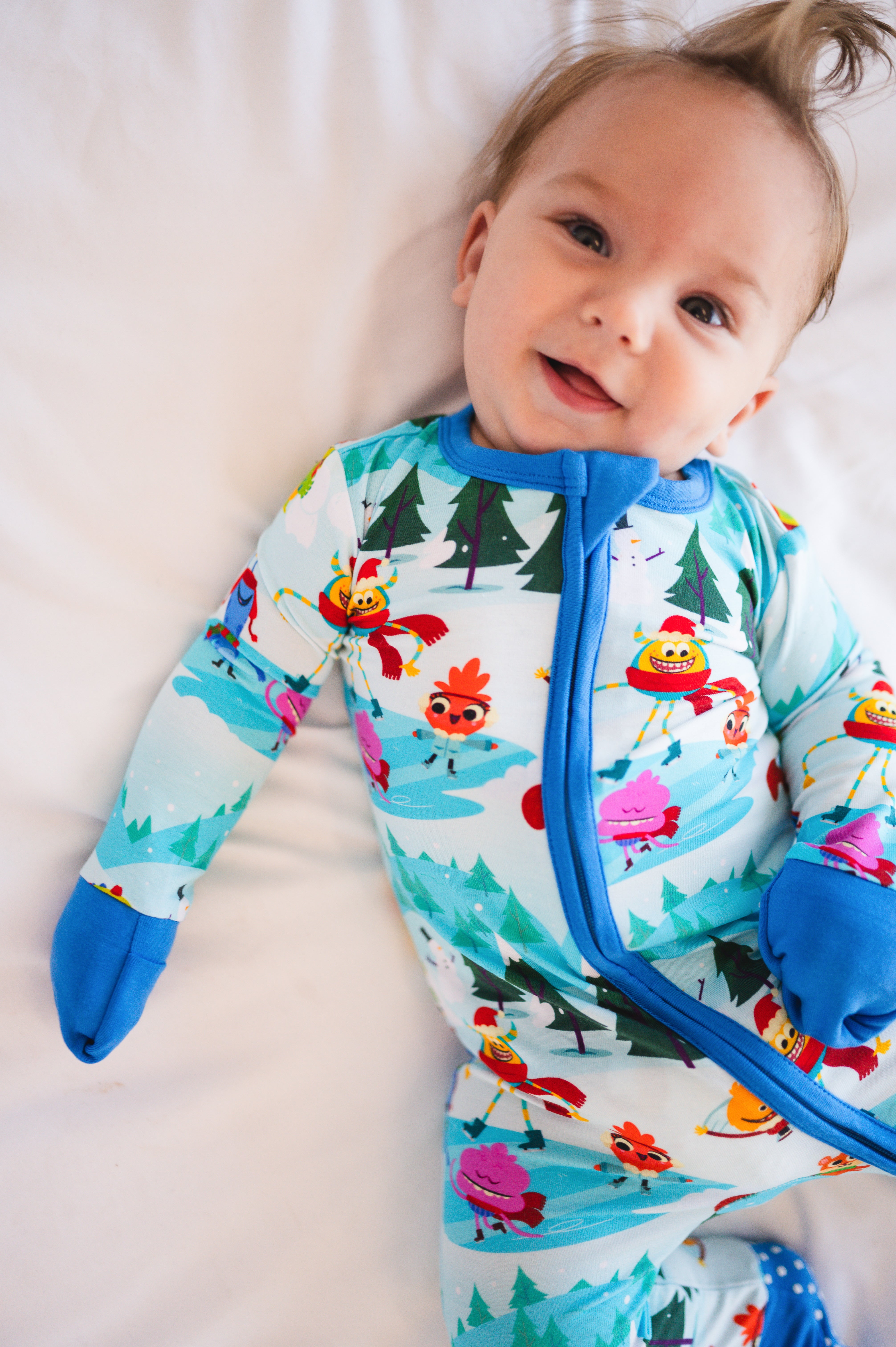 A baby smiles in a light blue bamboo pajama set with a winter-themed print.