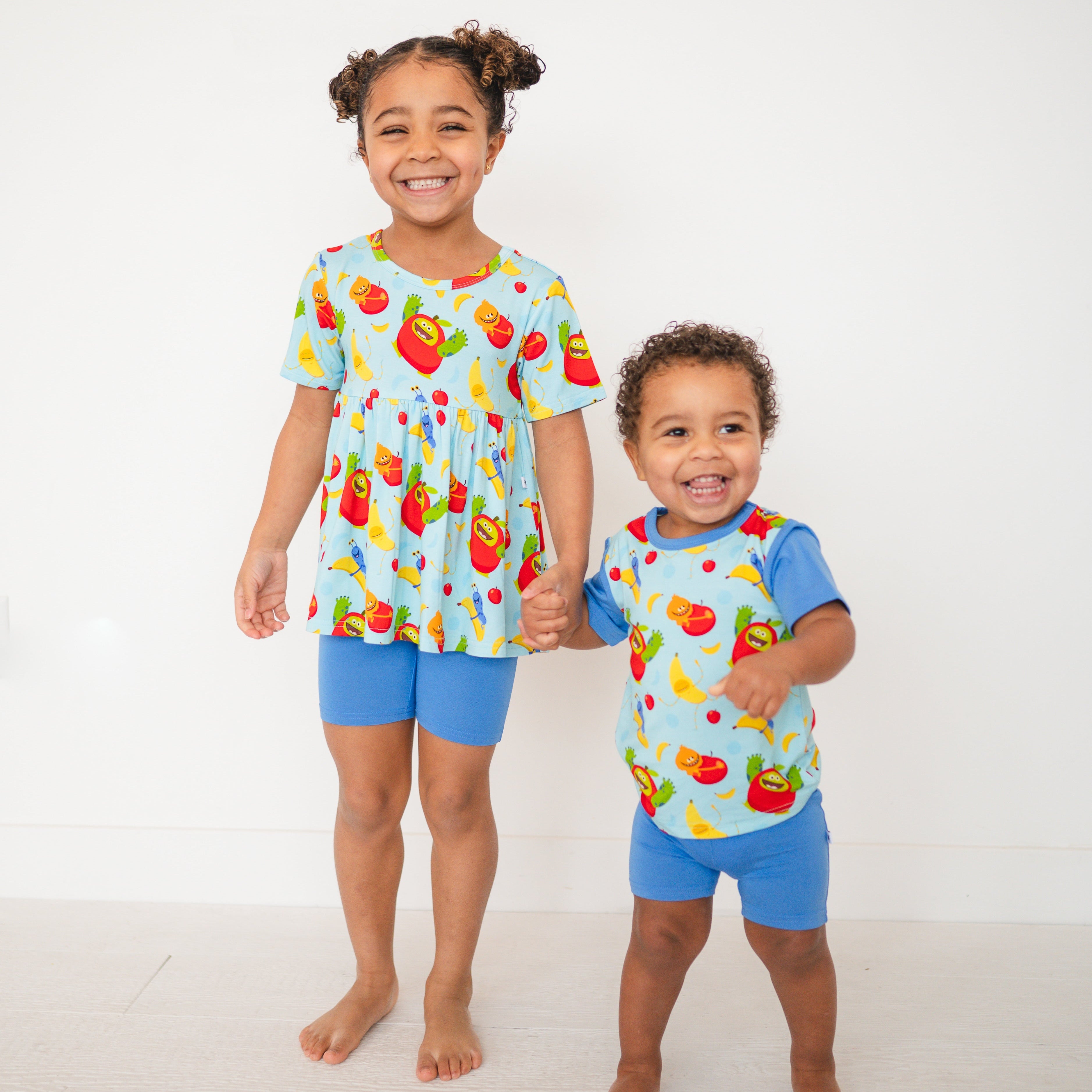 Two children in blue pajamas with a fruit pattern, holding hands.