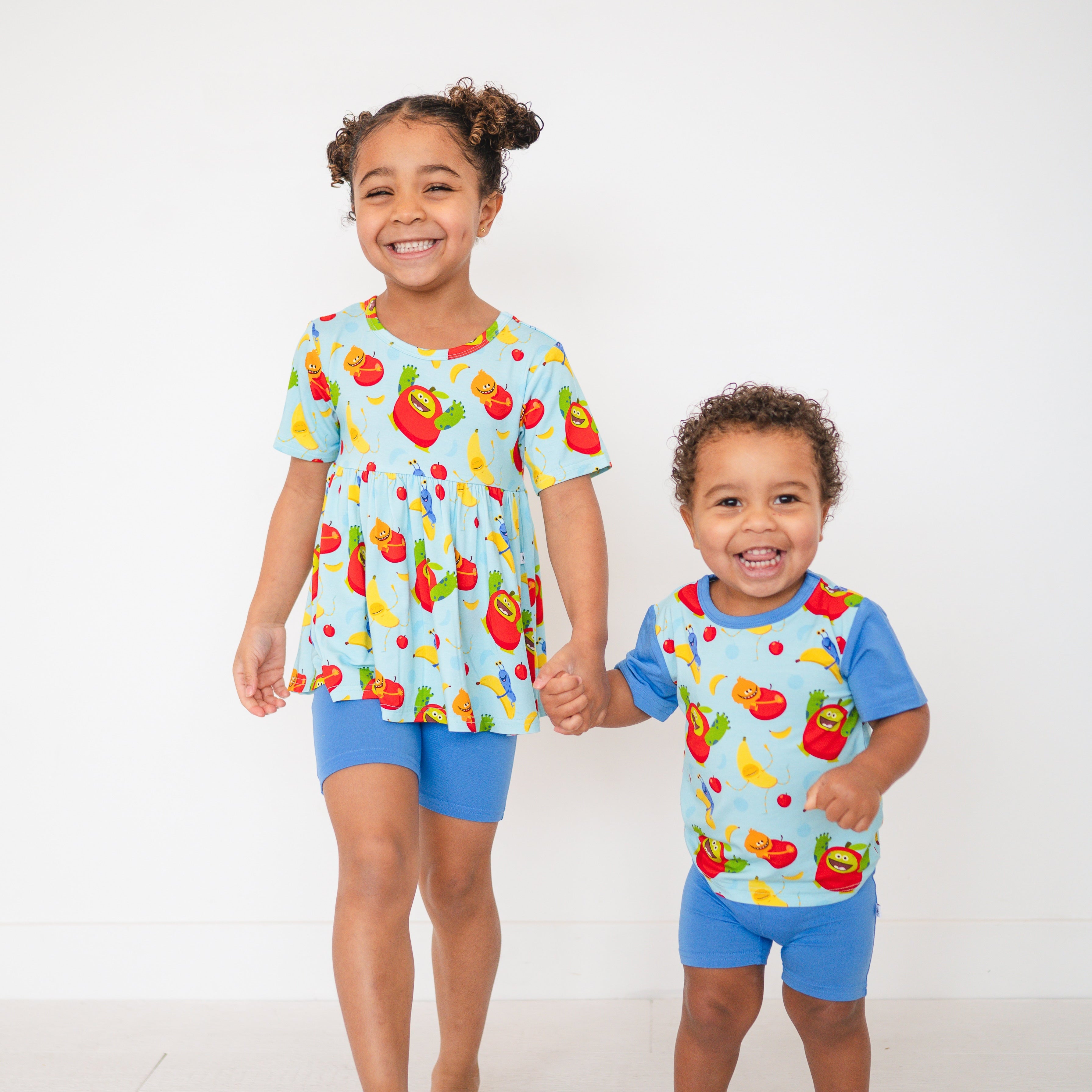 Two children in light blue t-shirts and shorts with a fruit pattern.