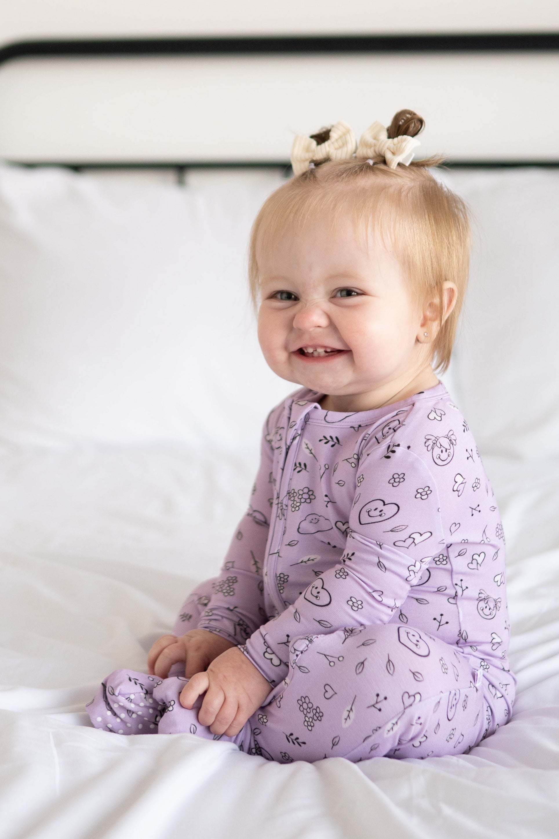 A baby girl smiles while wearing a lilac bamboo pajama set with a doodle print.