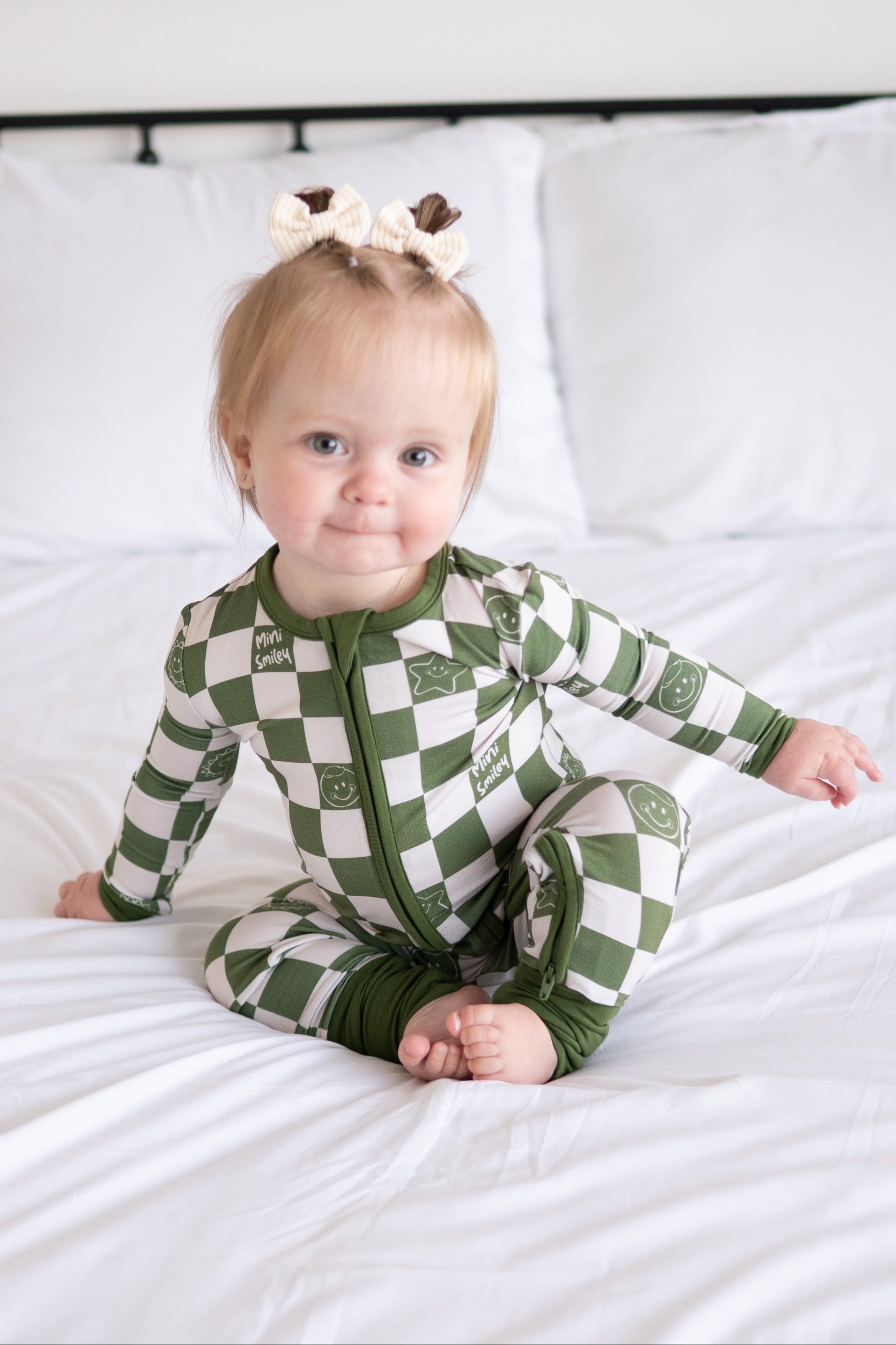 A baby wearing a green and white checkered bamboo pajama set with smiley faces.