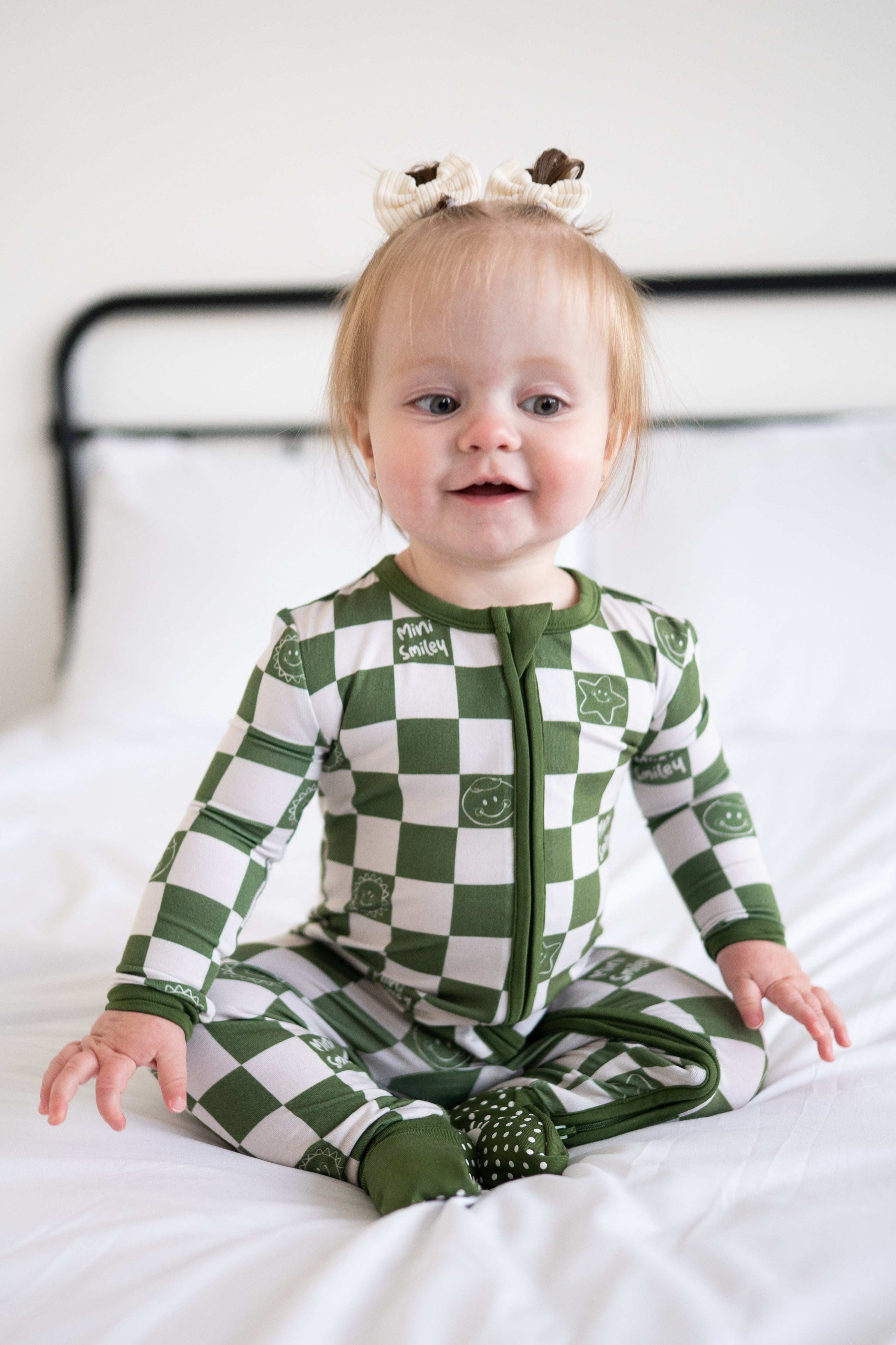 A baby wearing a green and white checkered bamboo pajama set with smiley faces.