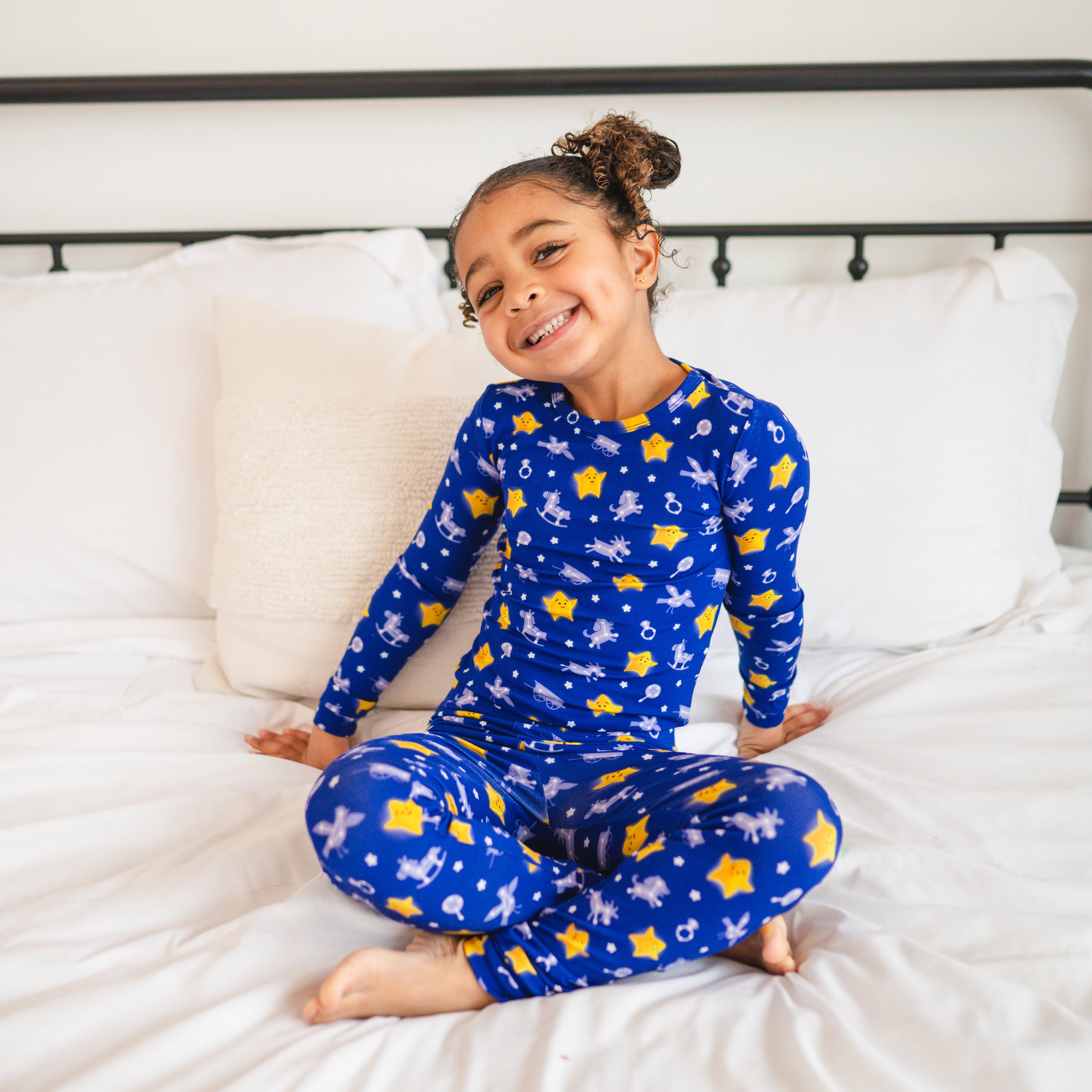 A young girl smiles in blue pajamas with yellow stars and white toy patterns.