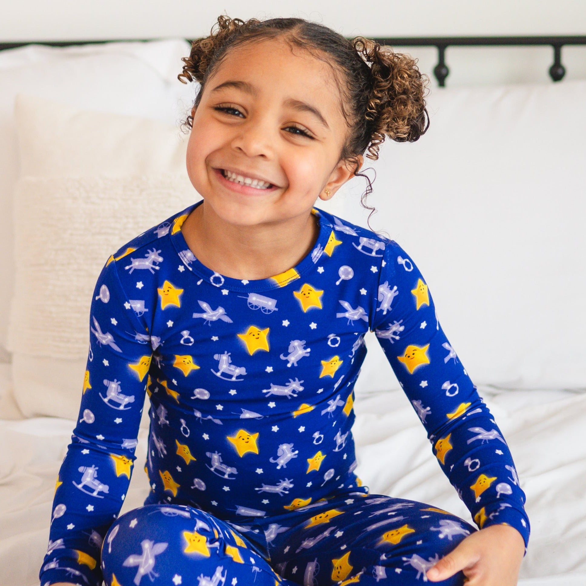 A young girl smiles in blue pajamas with a star and rocking horse pattern.