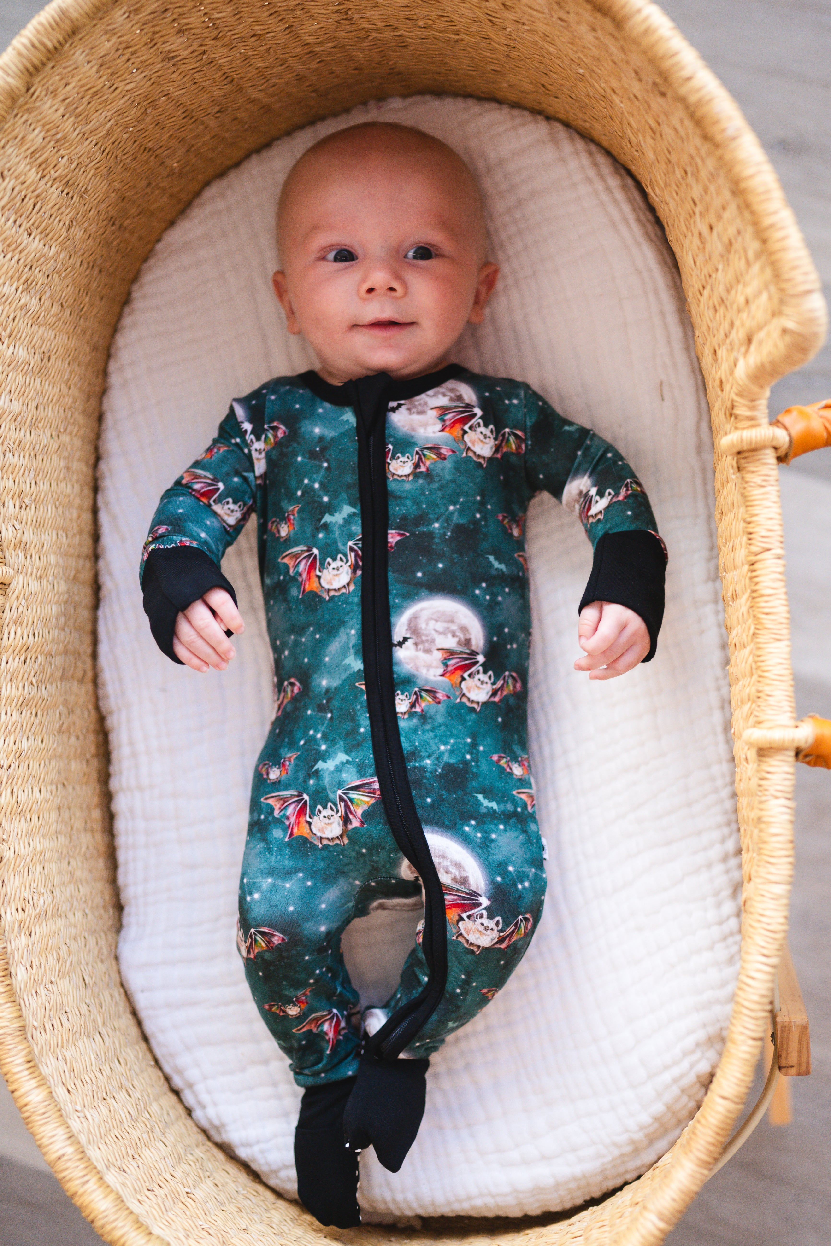 Baby in a bamboo zip pajama with a bat and moon print.