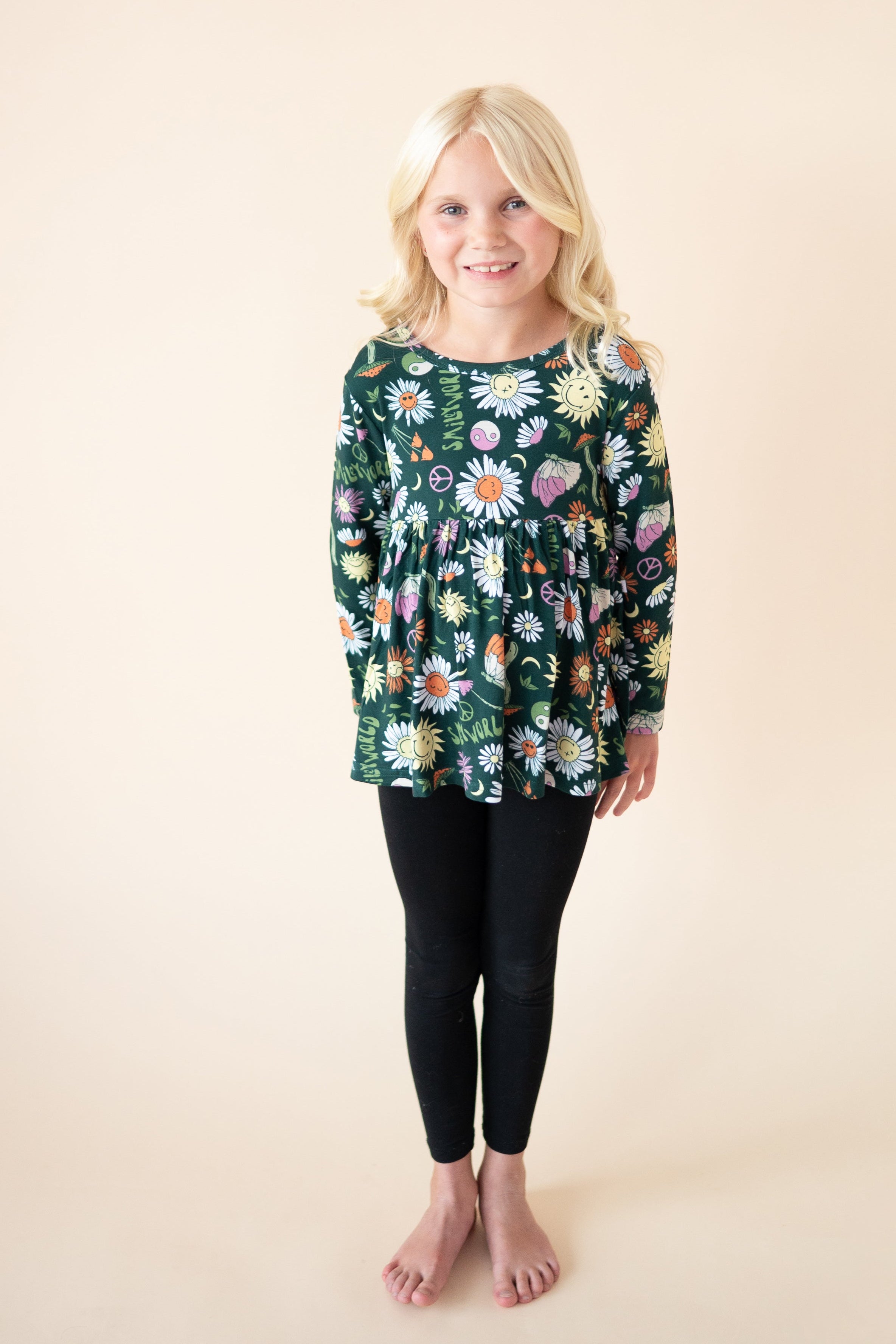 Girl wearing a long-sleeve peplum top with a green floral and smiley face print.