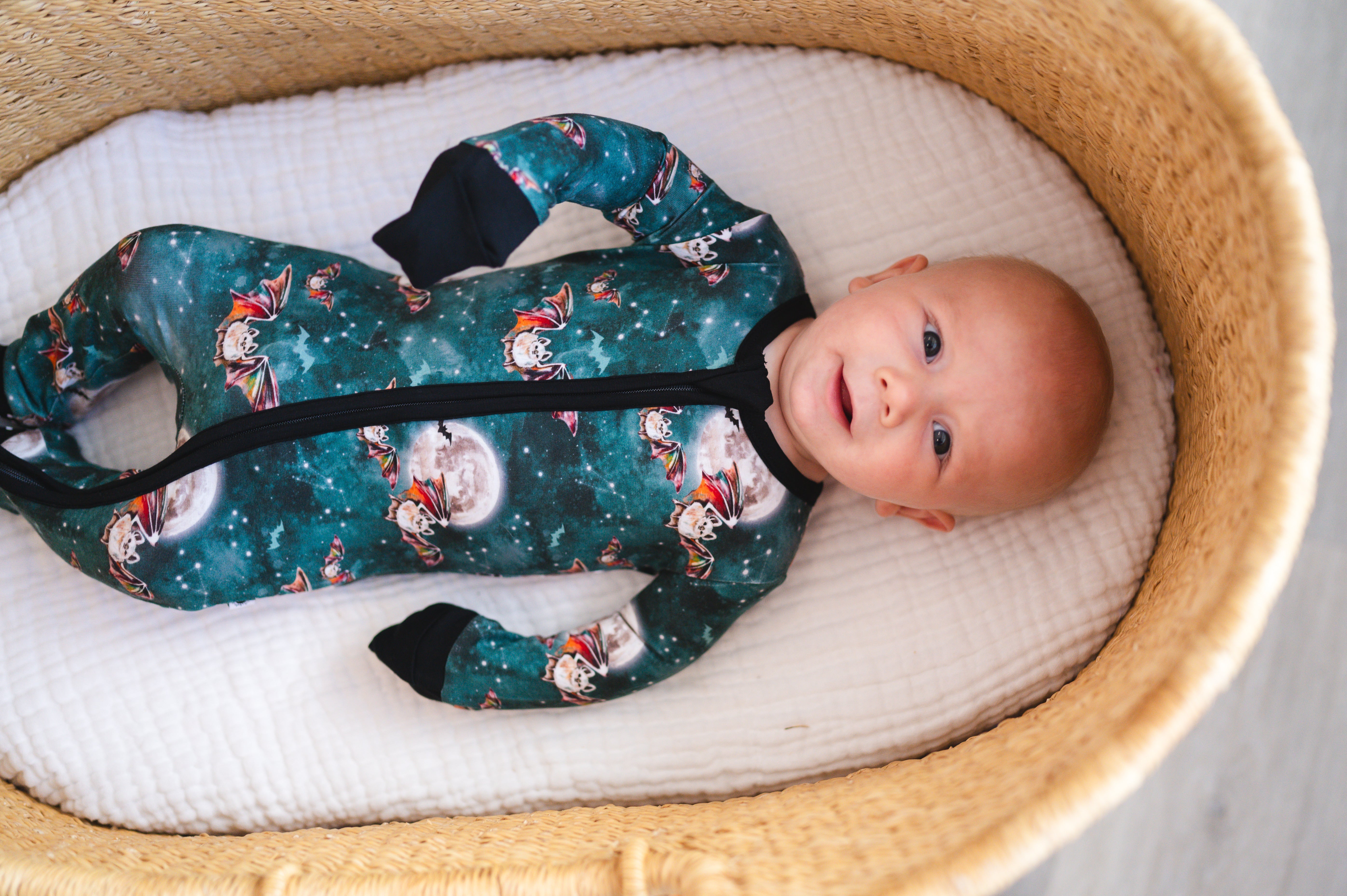 Baby in a teal bamboo pajama set with a bat and moon print.