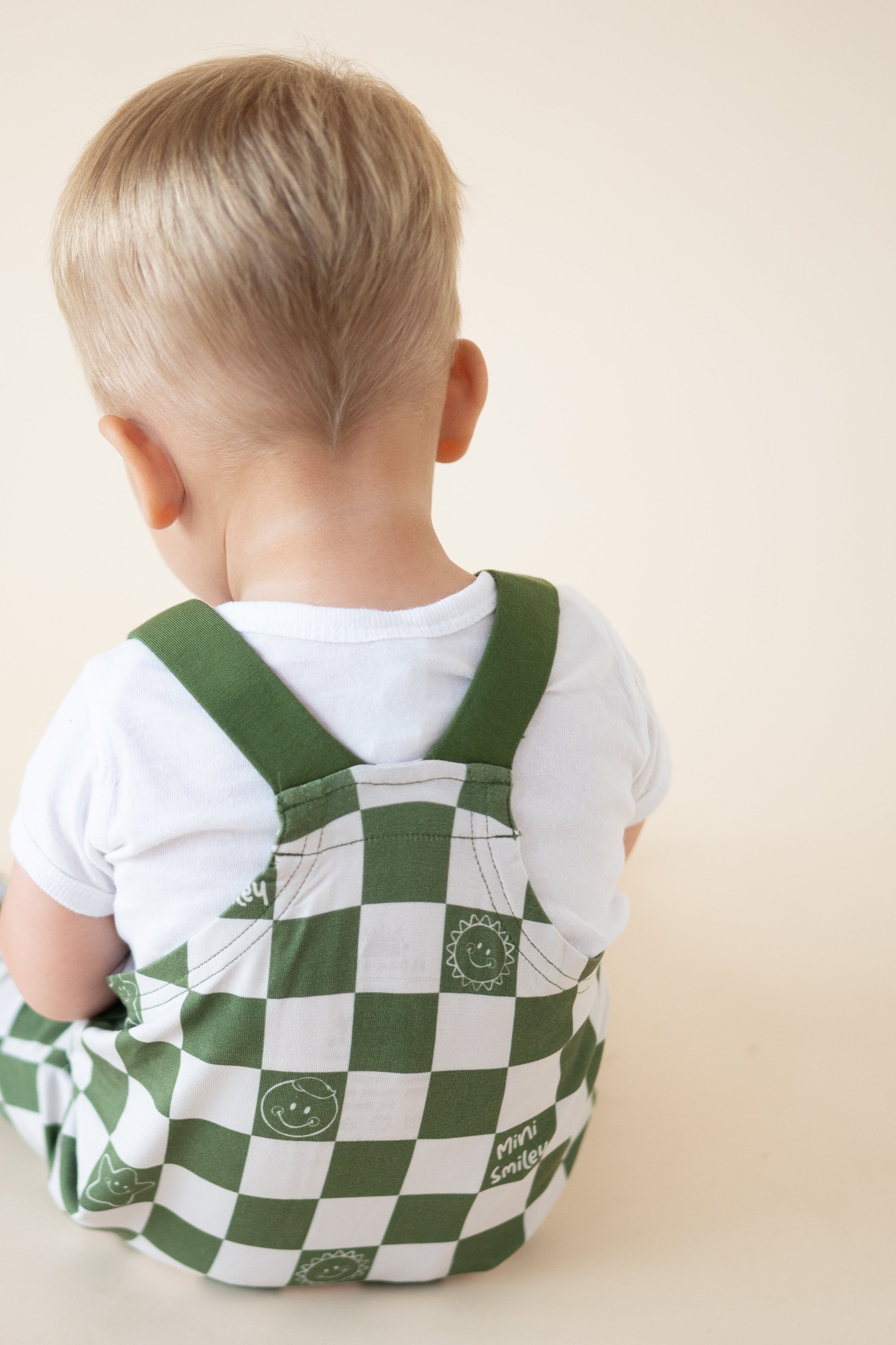 Baby overalls with a green and white checkerboard pattern and smiley face graphics.