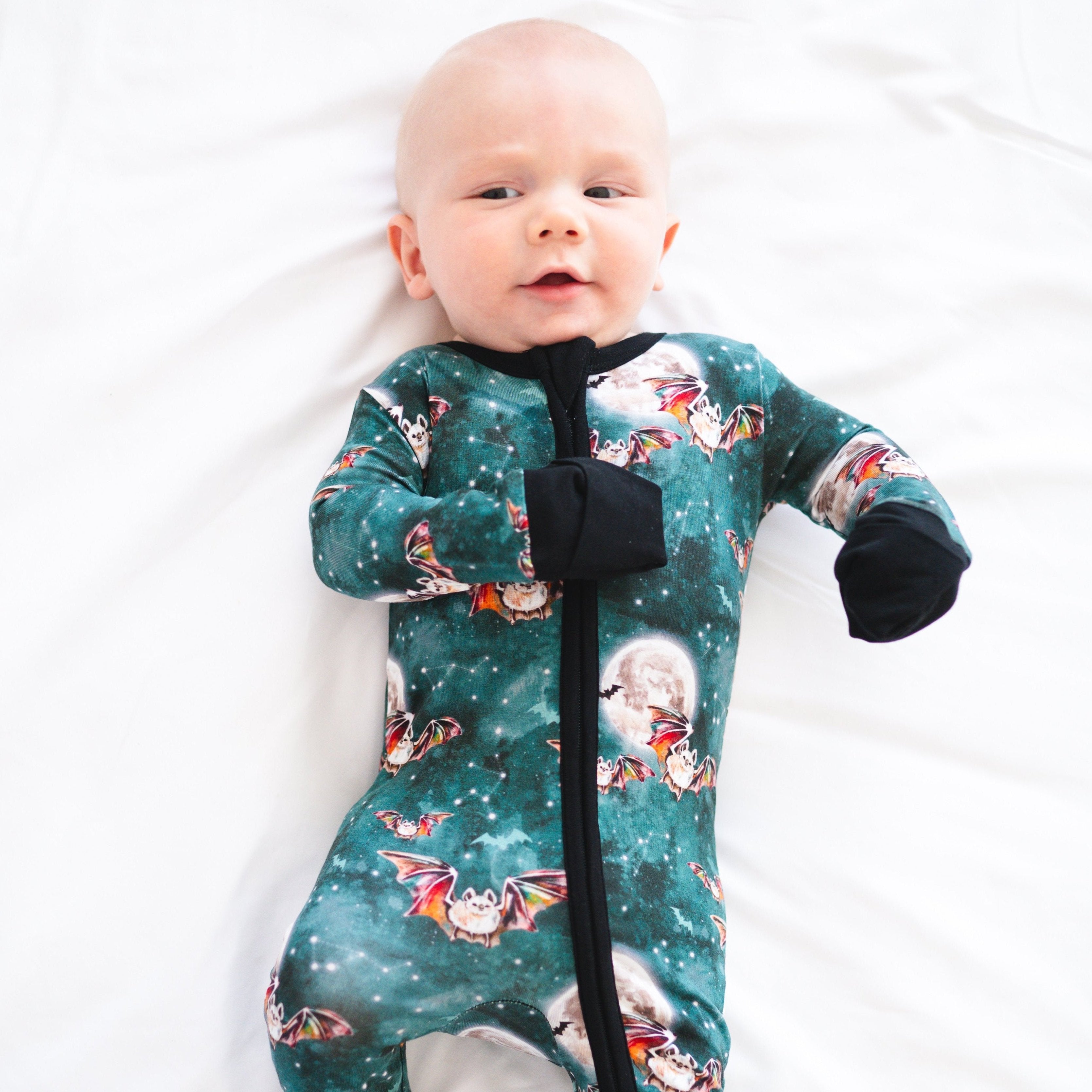 A baby wearing a teal bamboo pajama set with a bat and moon print.