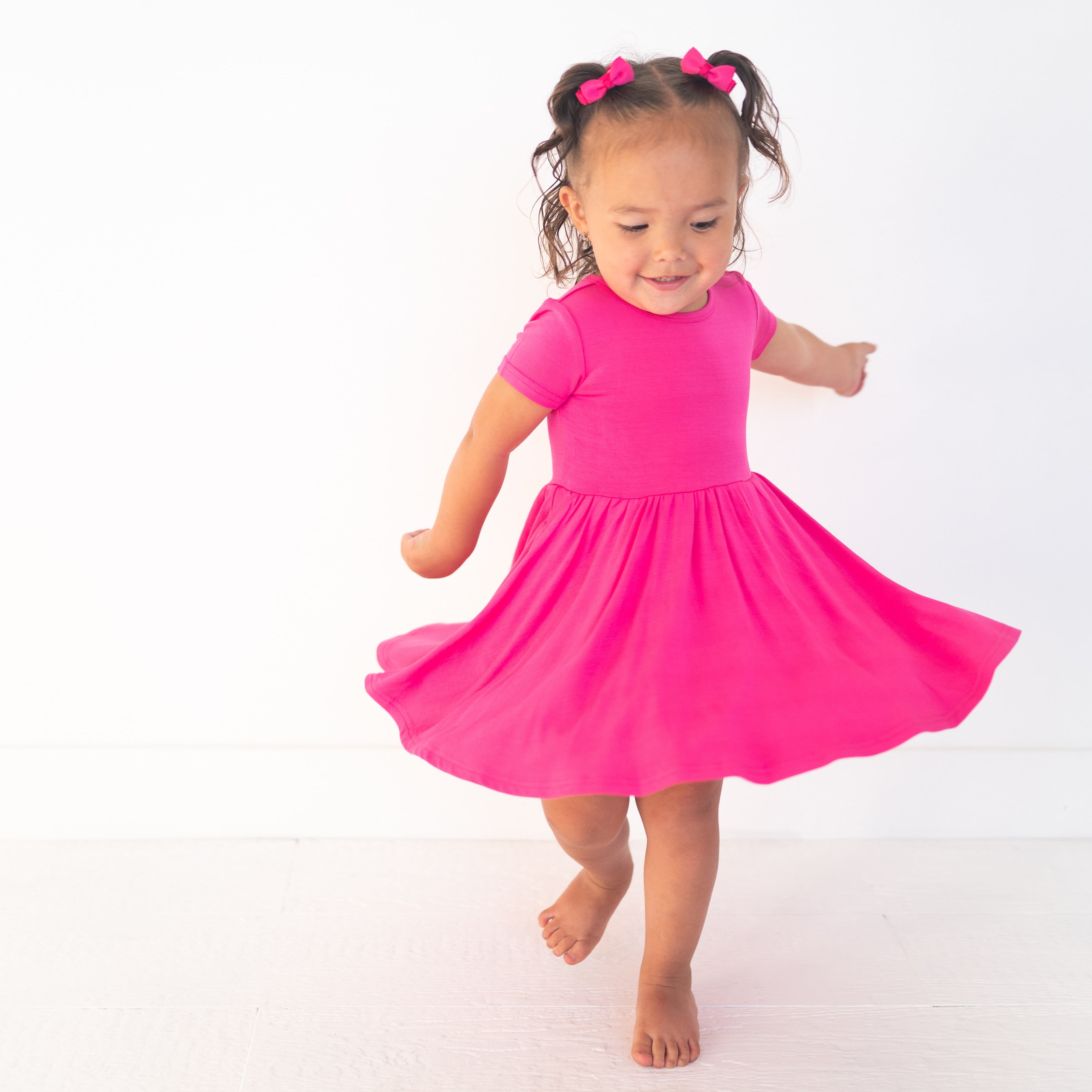 A young girl in a pink dress with bows in her hair twirls.