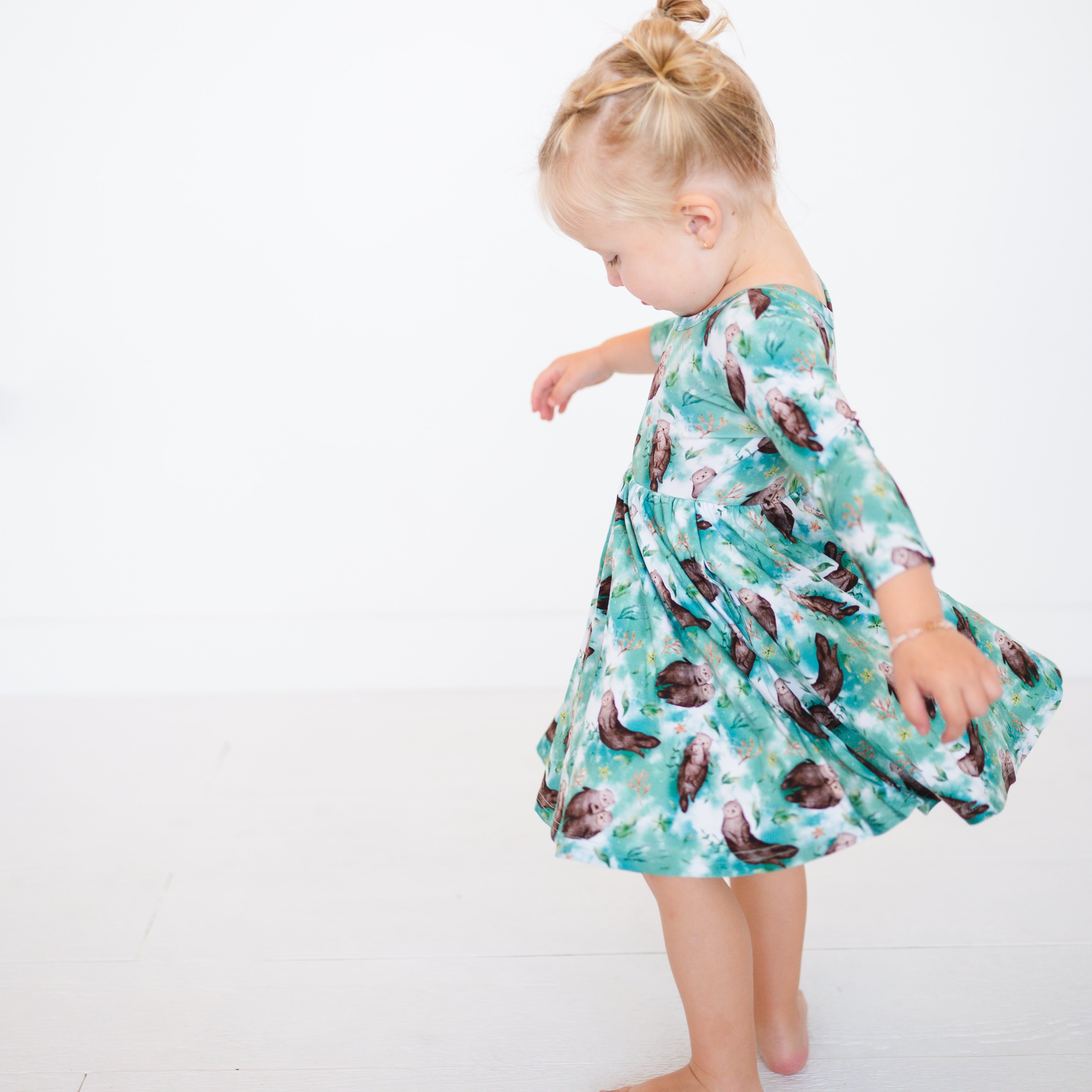 A young girl in a teal dress with an otter print twirls against a white background.