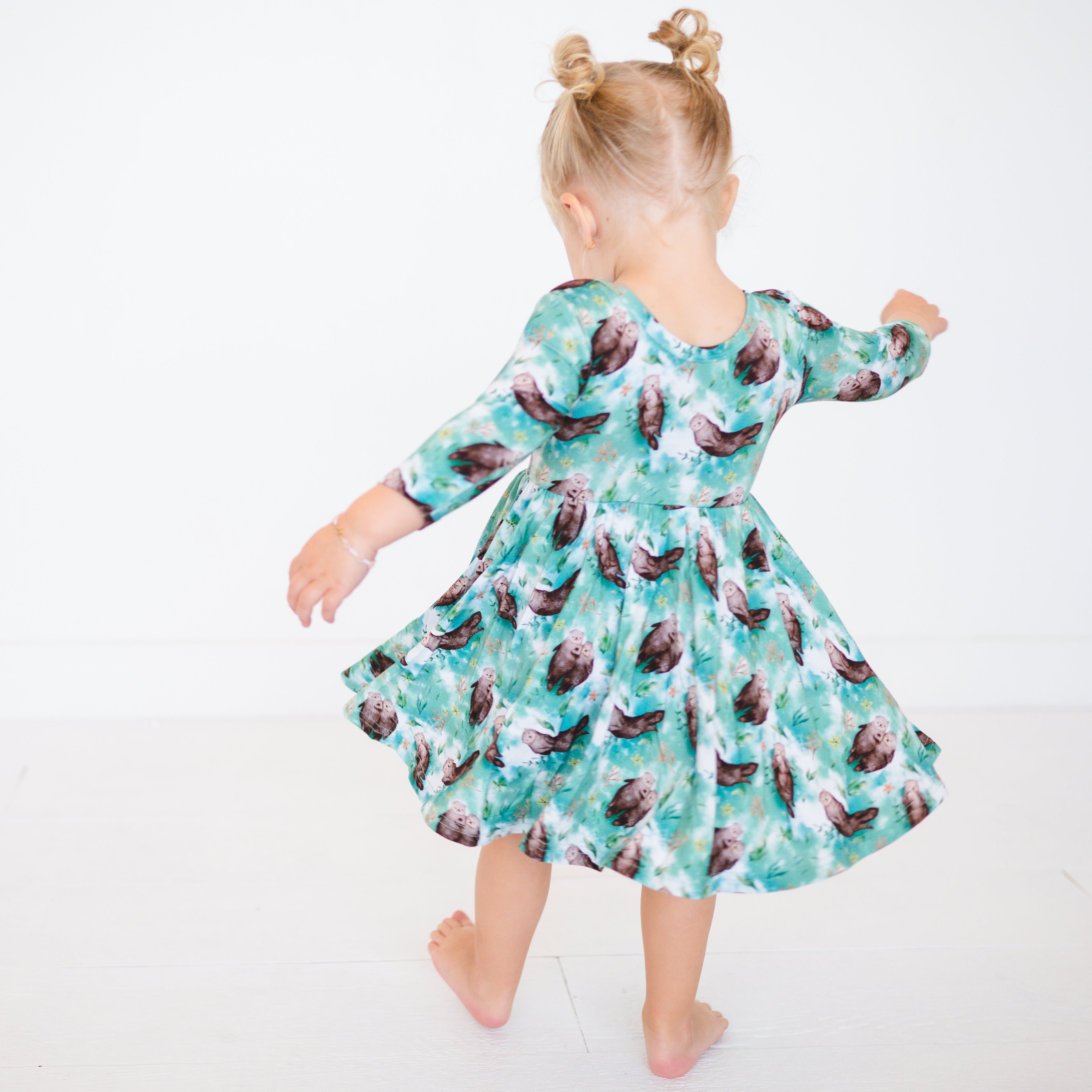 A girl in a teal dress with an otter print twirls against a white background.