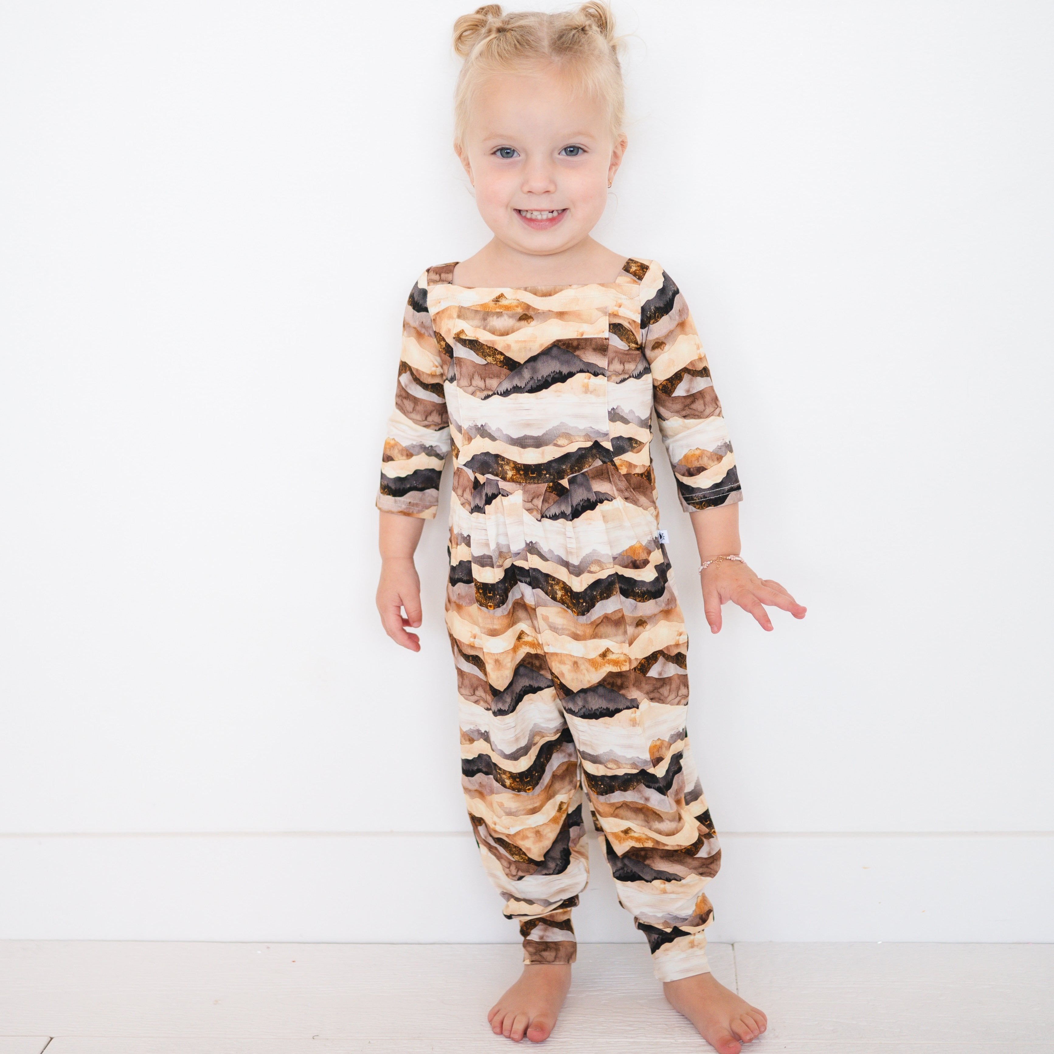 A young girl wears a brown and tan mountain range print bamboo romper.