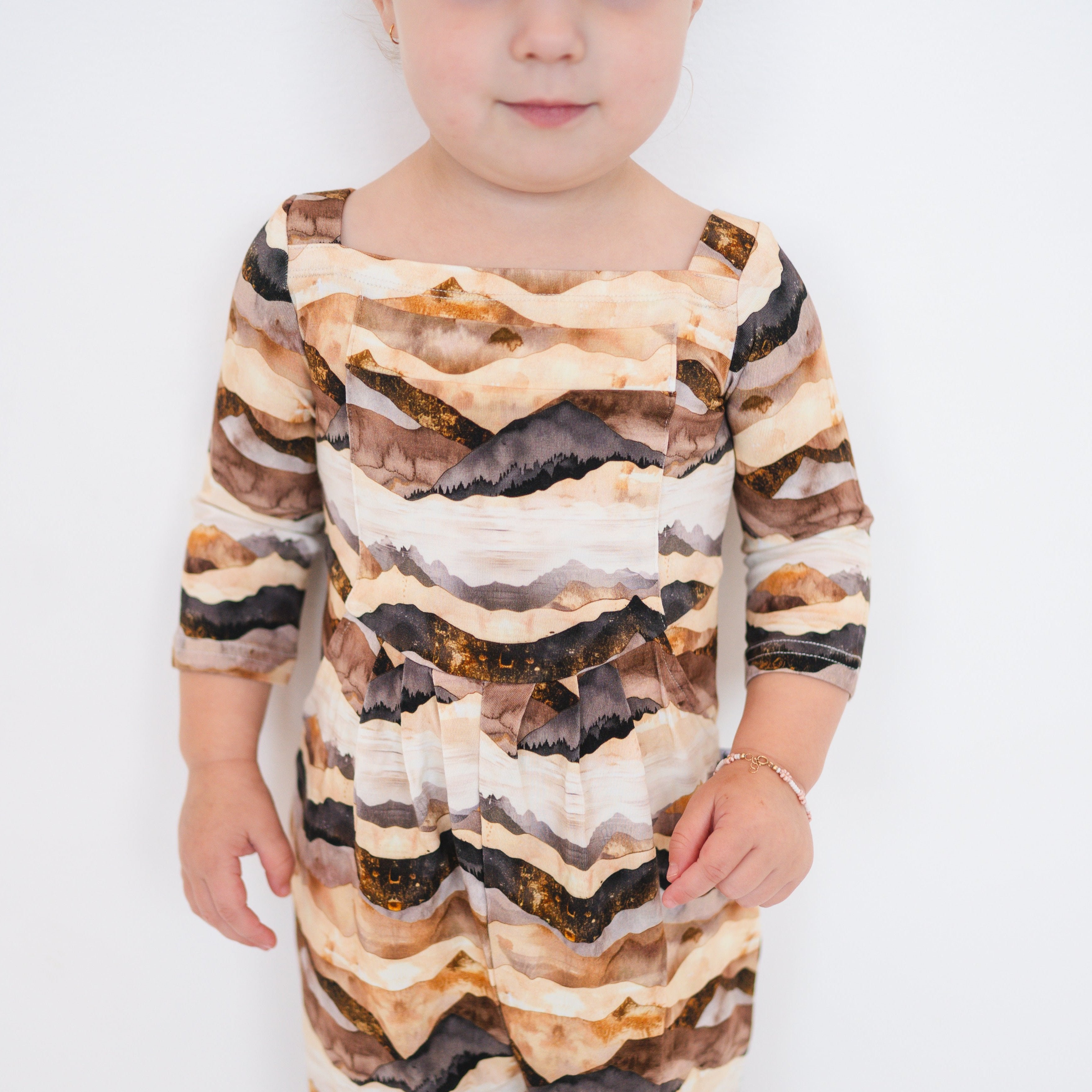 A child wears a long-sleeved romper with a mountain range print.