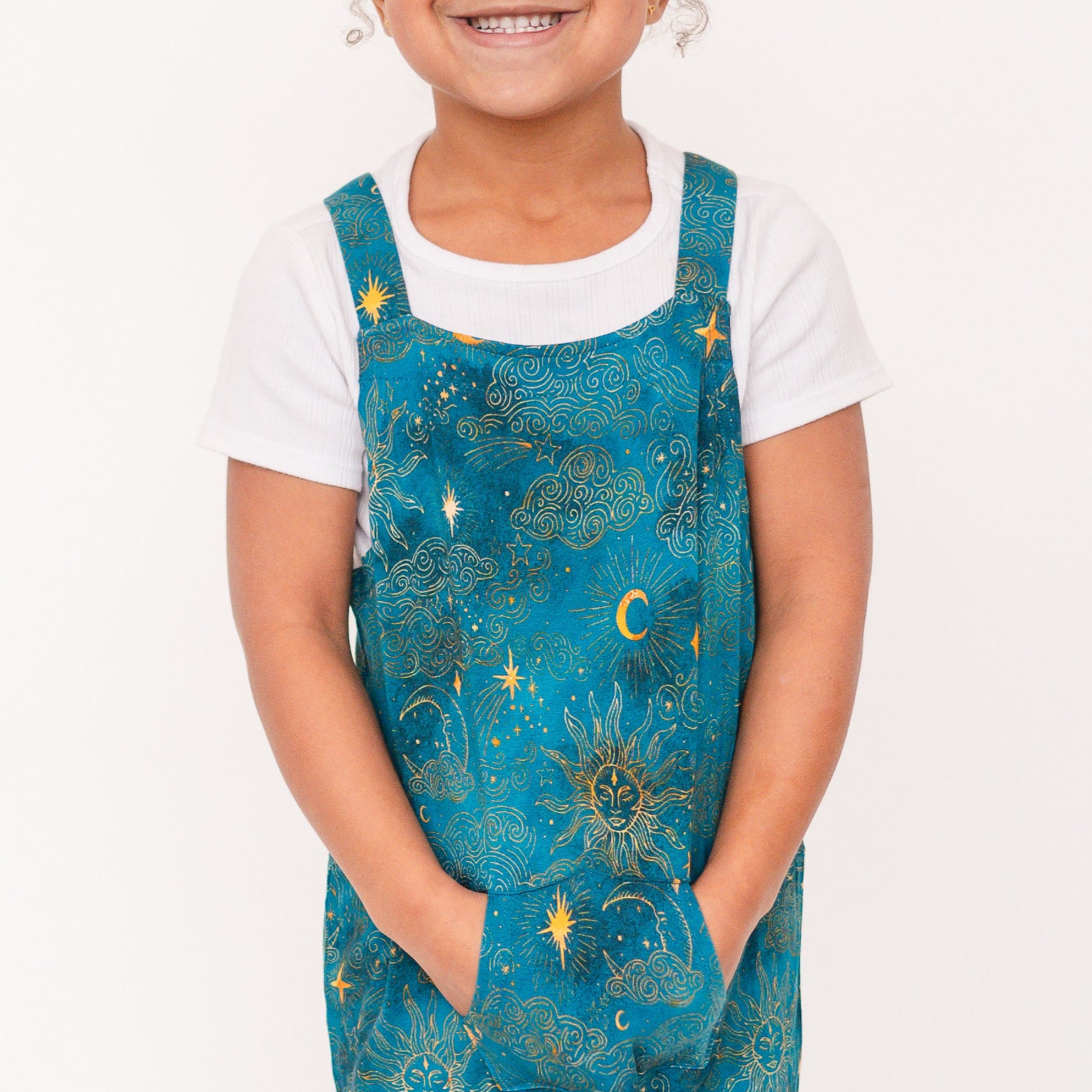 A child wears teal overalls with a celestial print over a white t-shirt.
