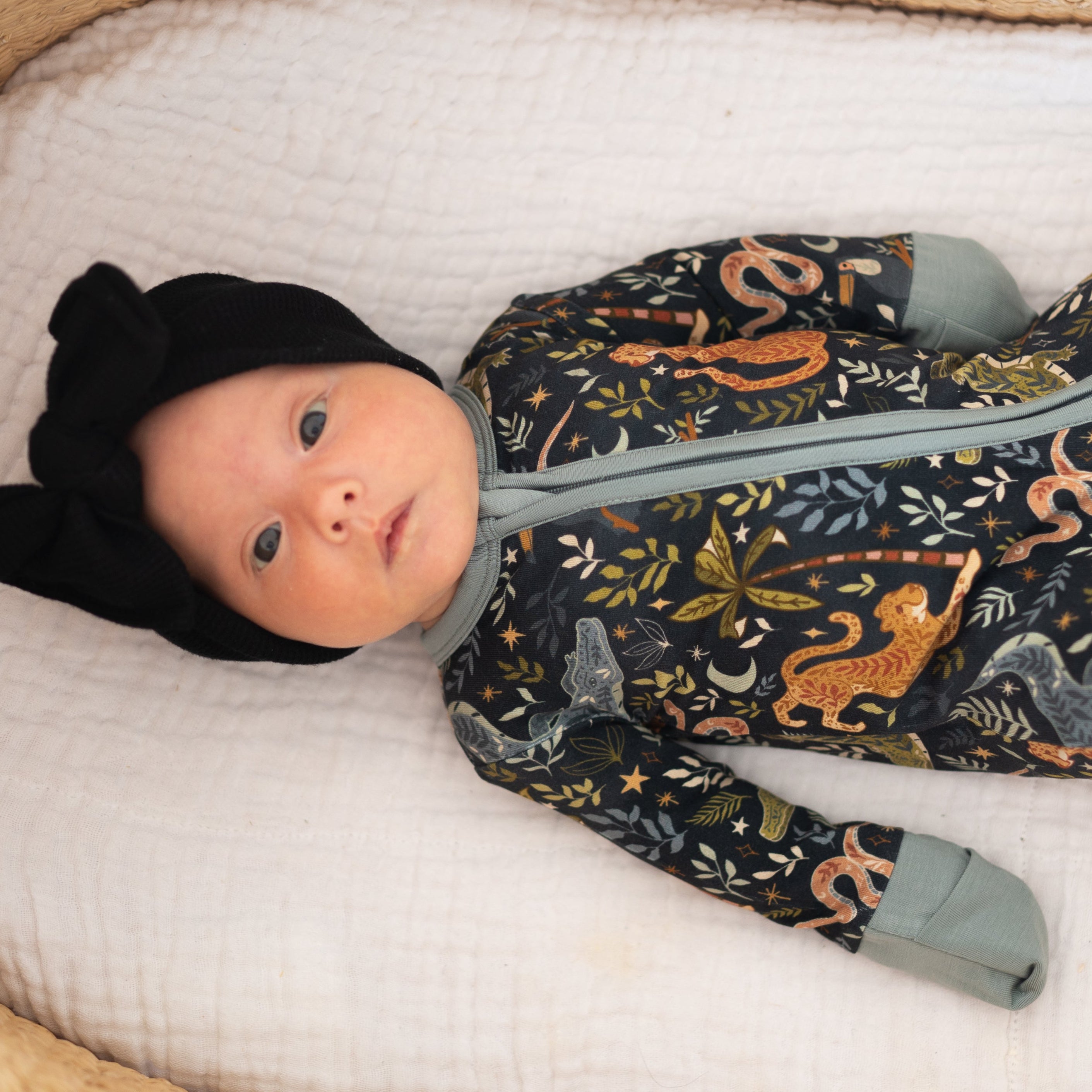 Baby in a black bow hat and a dark blue pajama set with a jungle print.