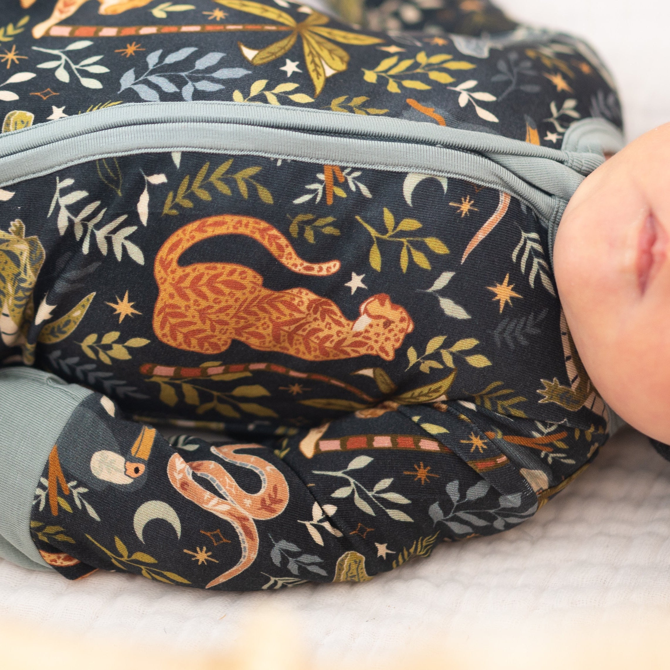 A baby wearing a dark blue pajama set with a jungle print featuring leopards and snakes.