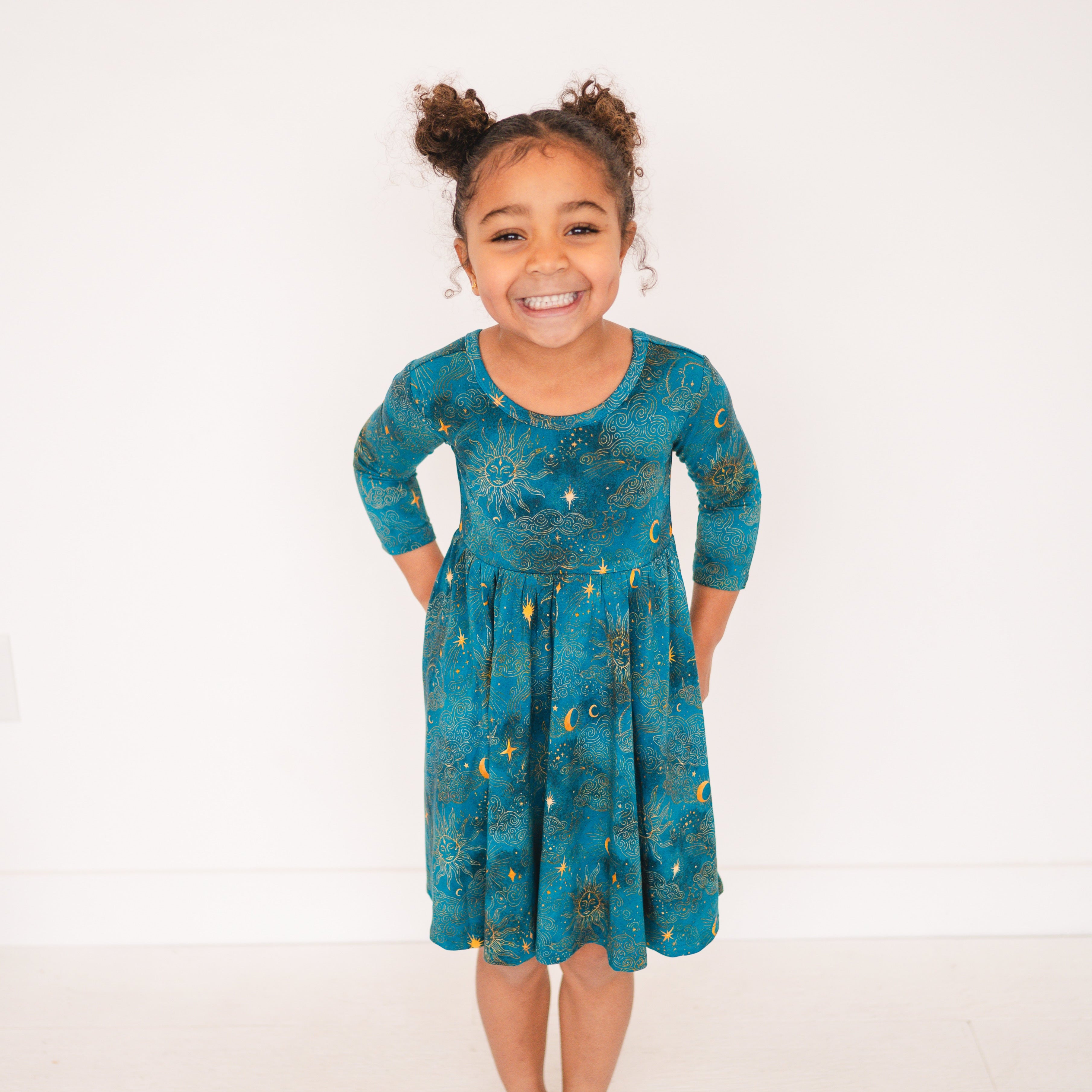 A young girl wears a teal dress with a celestial print.