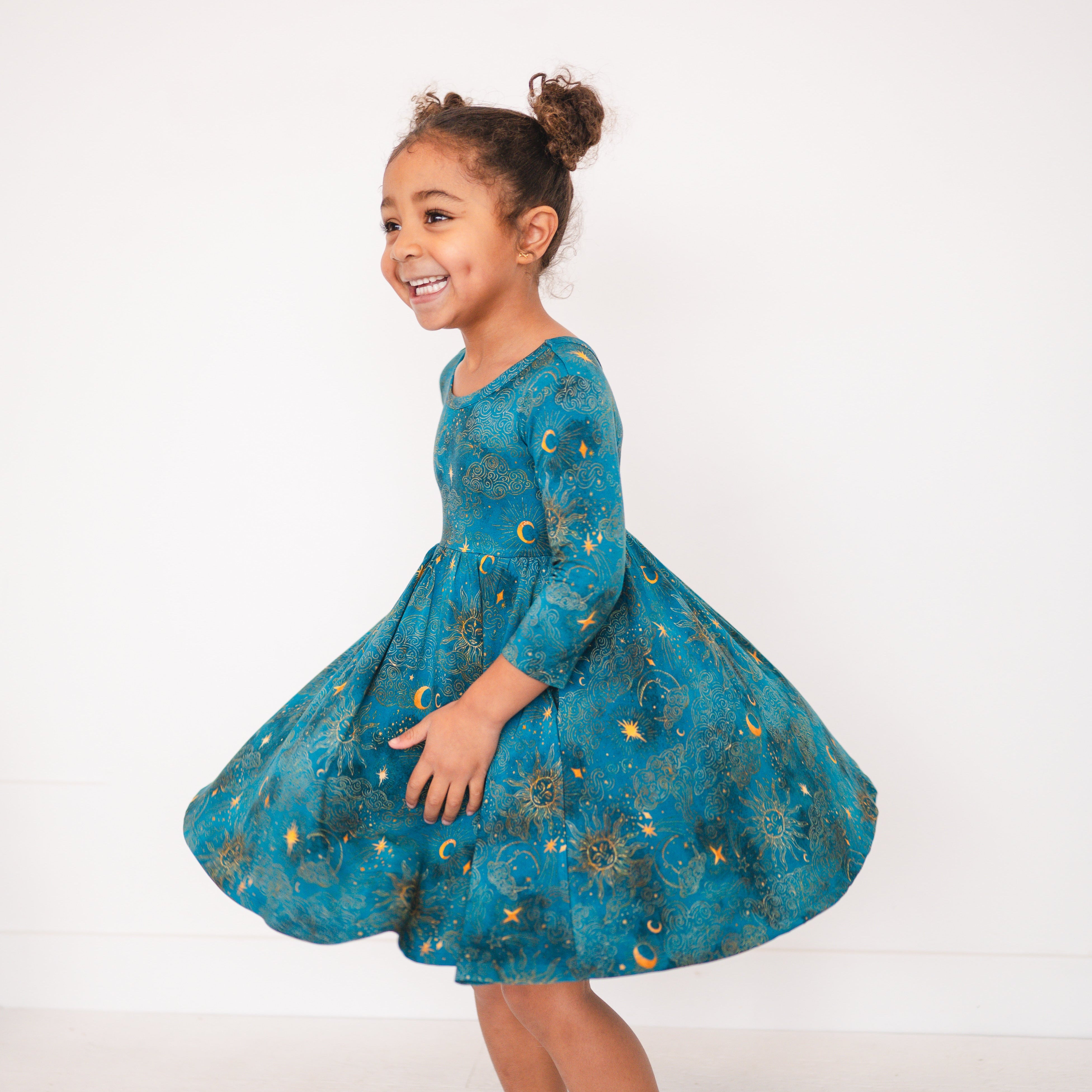 A young girl twirls in a teal dress with a celestial sun and moon print.