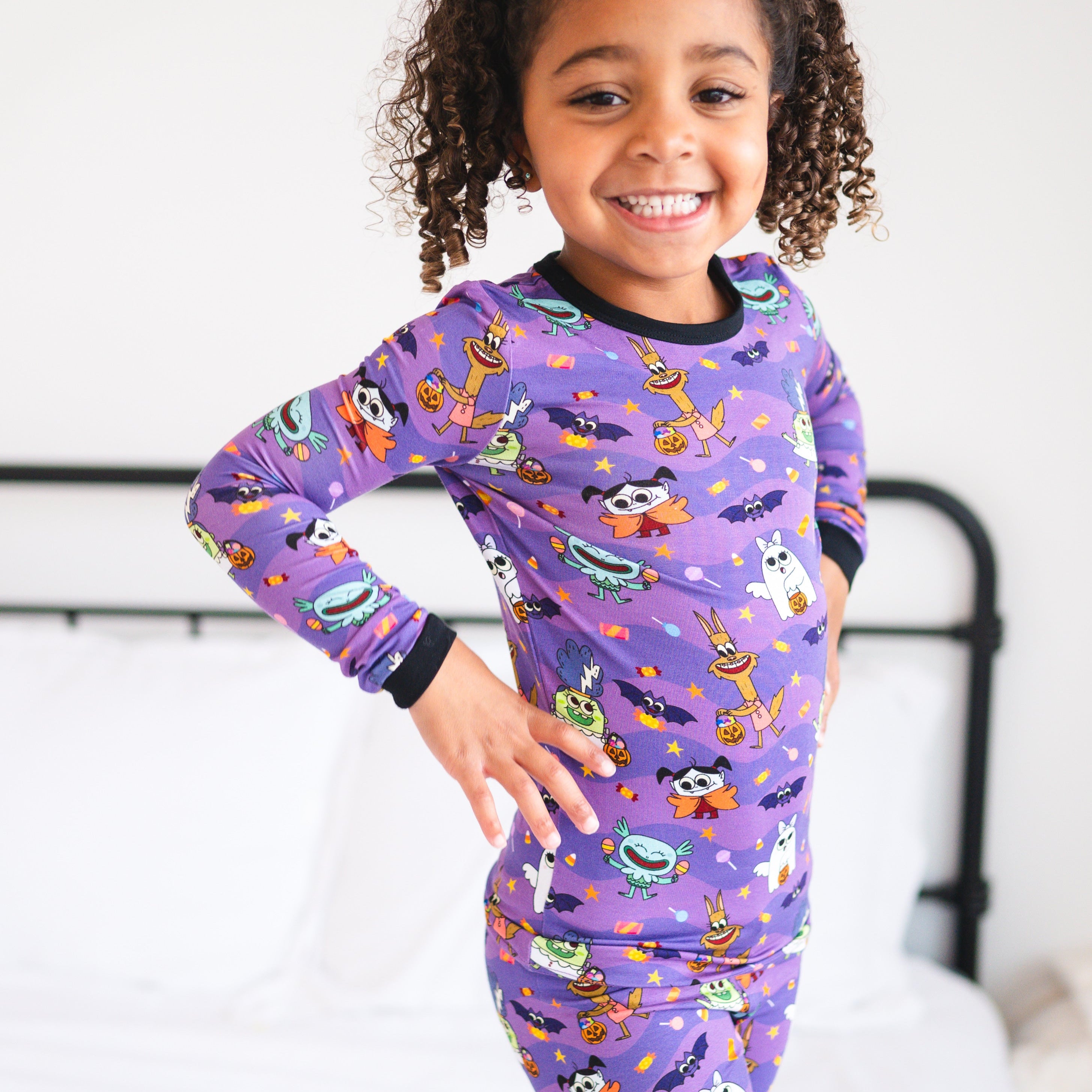 A young girl smiles wearing purple pajamas with a monster party print.