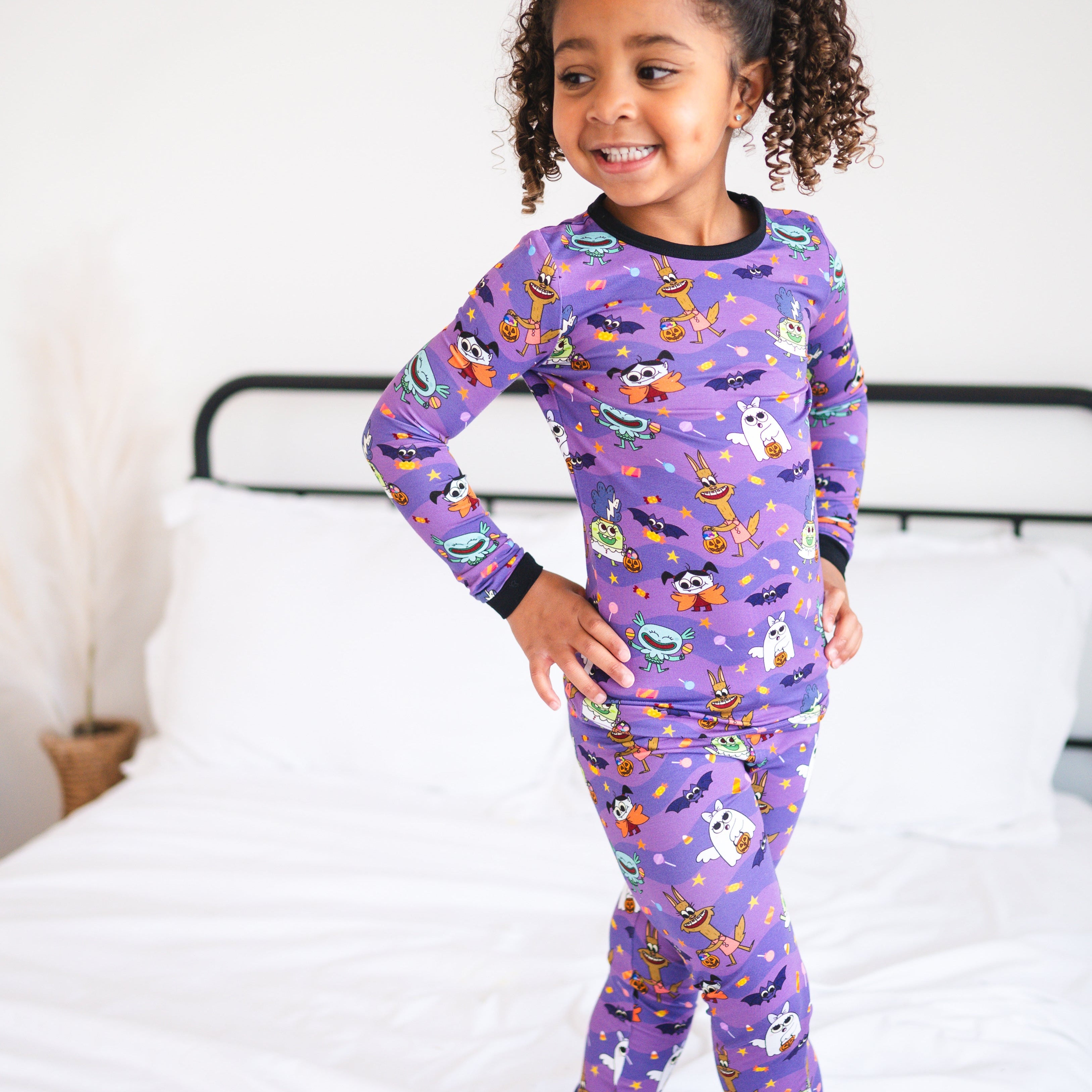 A young girl wears purple pajamas with a monster party print.