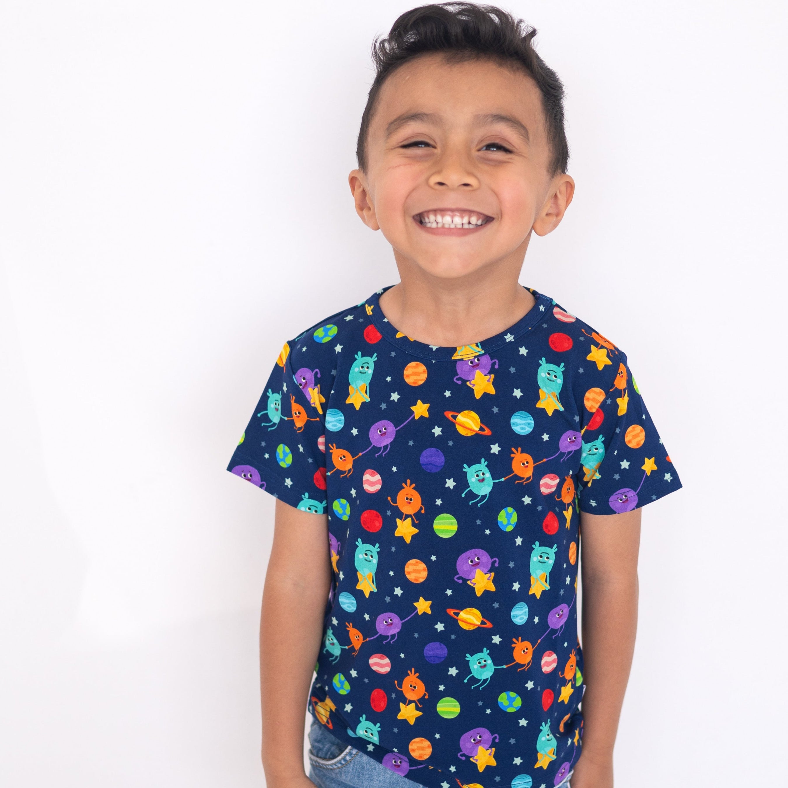 A young boy smiles wearing a navy blue t-shirt with a colorful space-themed print.