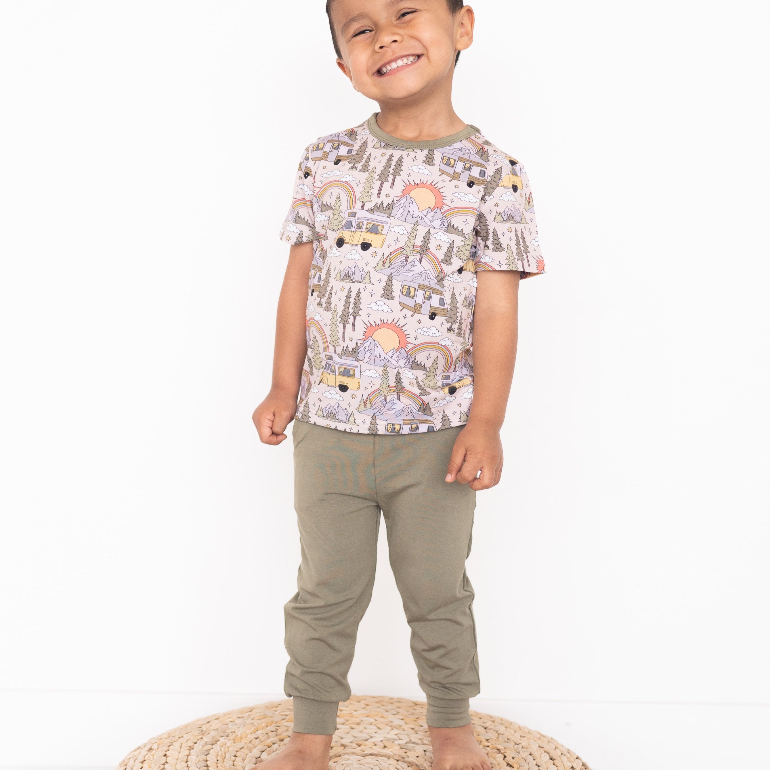 A young boy smiles while wearing a vintage camper print t-shirt and green joggers.