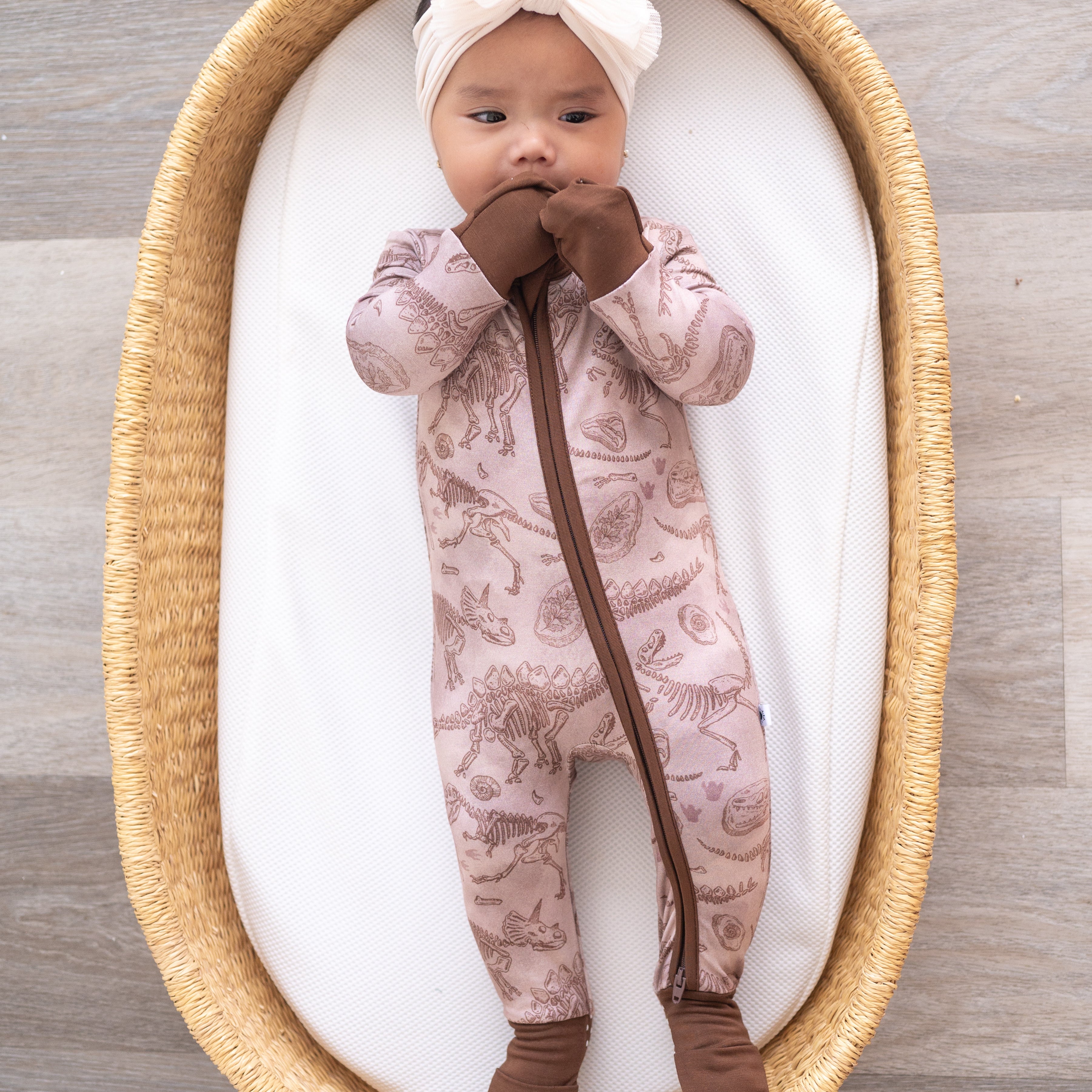 Baby in a pink bamboo pajama set with a fossil print, wearing a white headband.