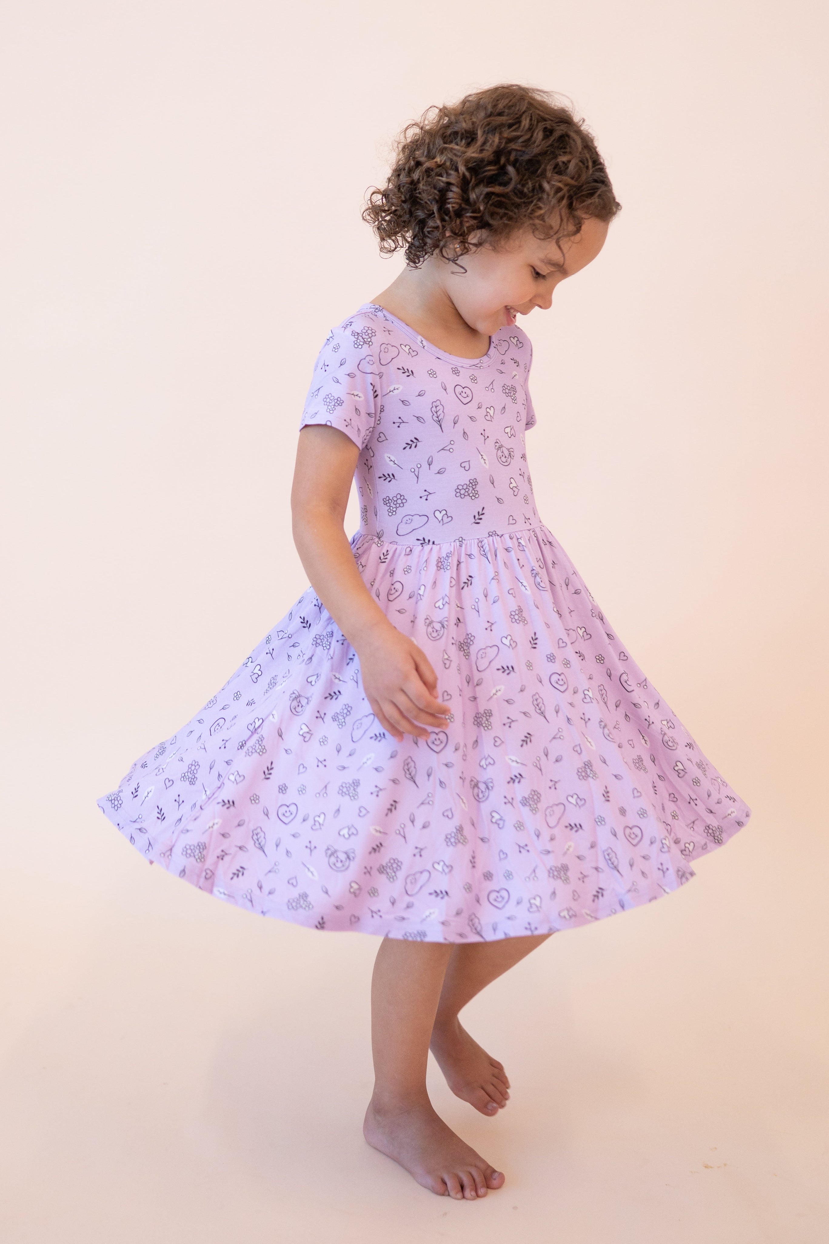 A young girl twirls in a lilac dress with a doodle print.