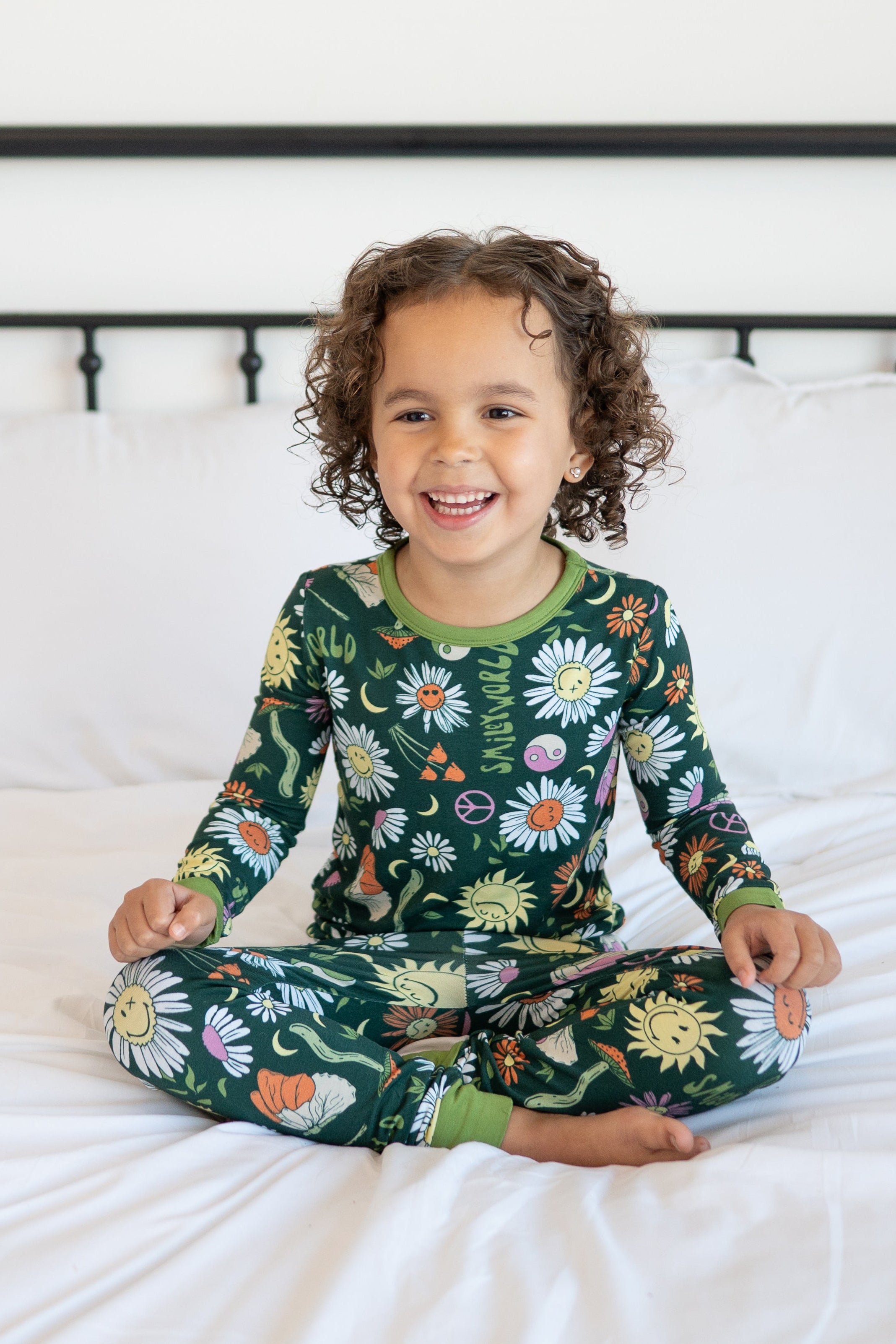 A young child smiles while wearing a green pajama set with a floral and smiley face print.