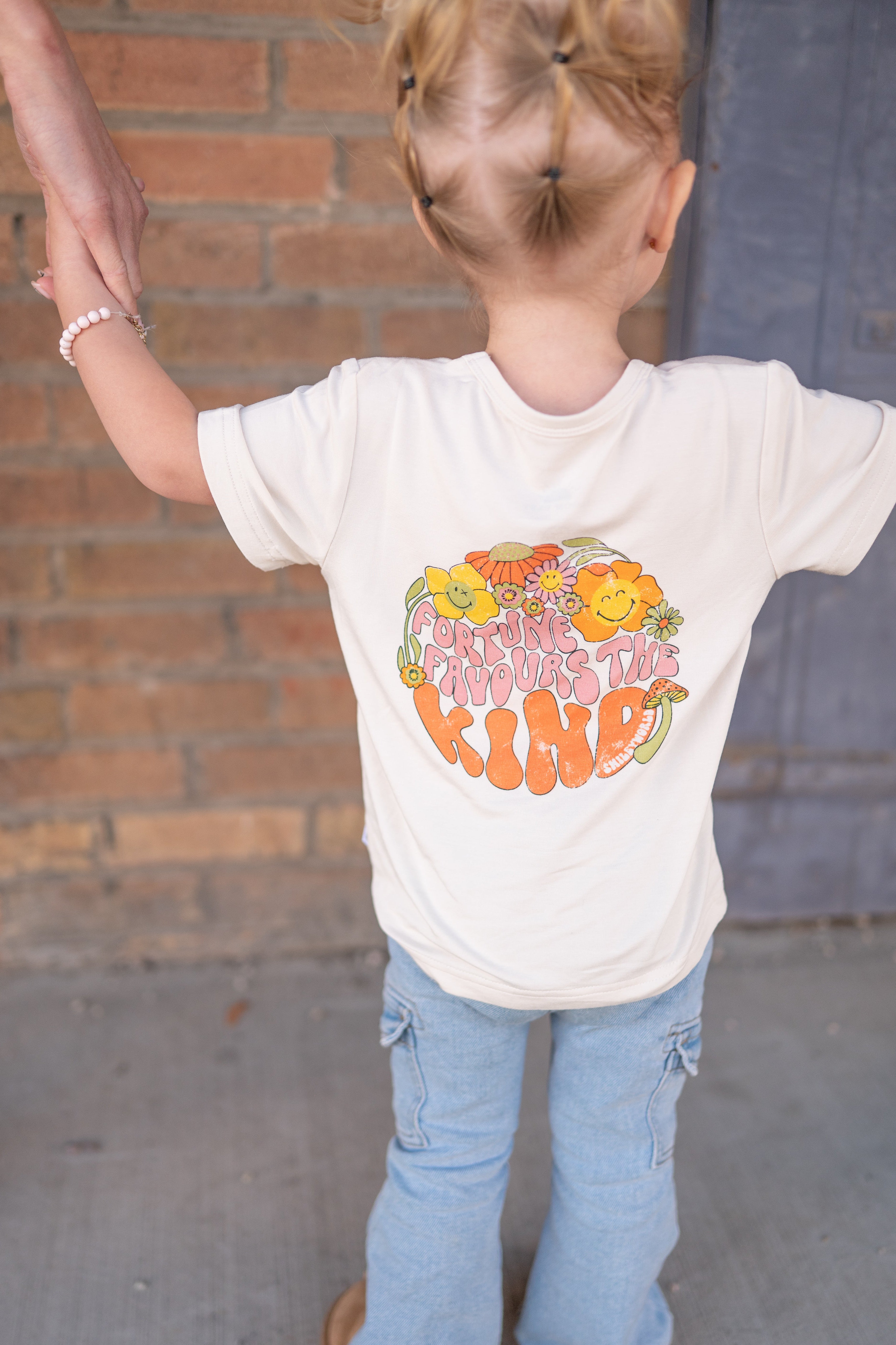 A child from behind wears a white t-shirt with "Fortune Favors the Kind" graphic.