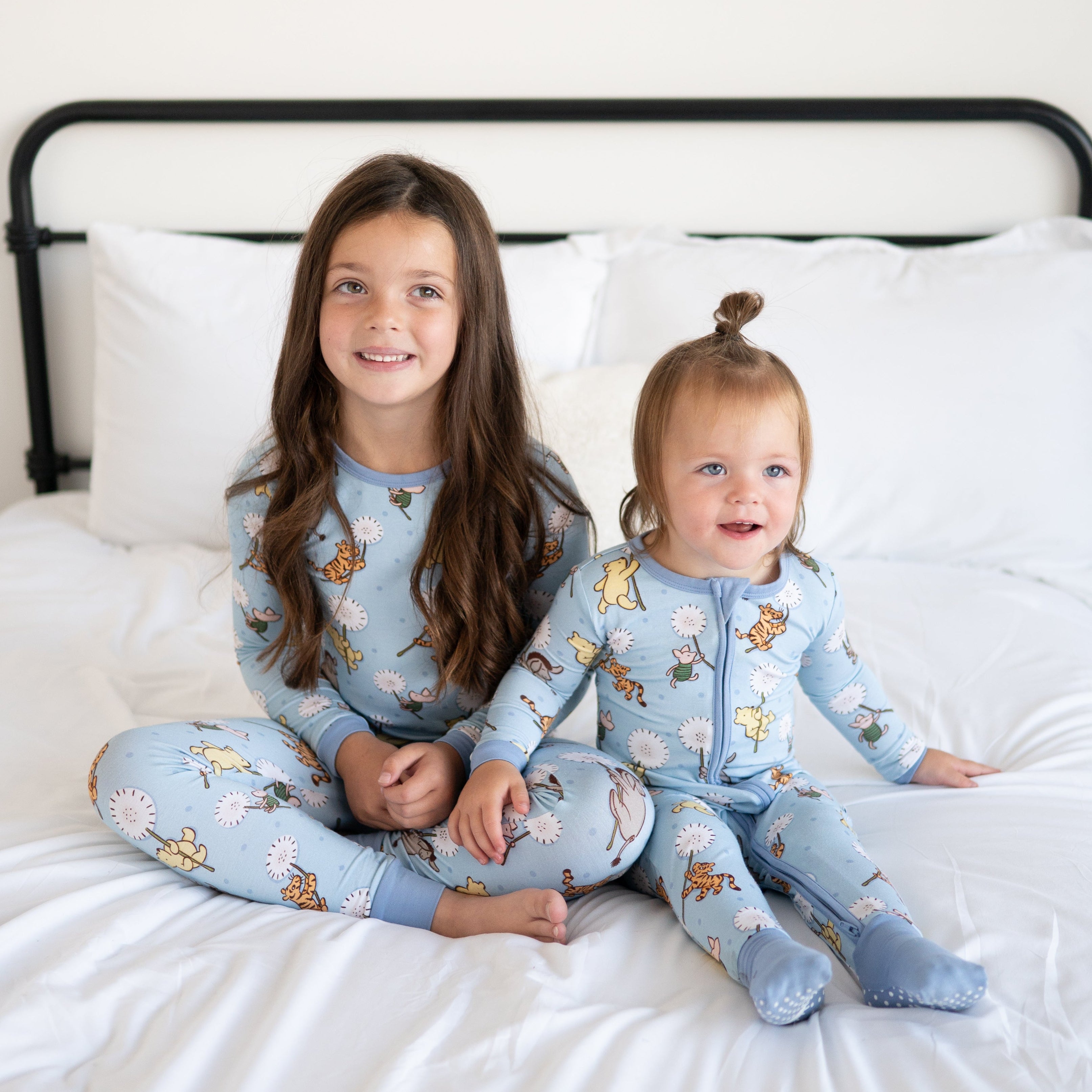 Two children in blue Winnie the Pooh pajamas sitting on a white bed.