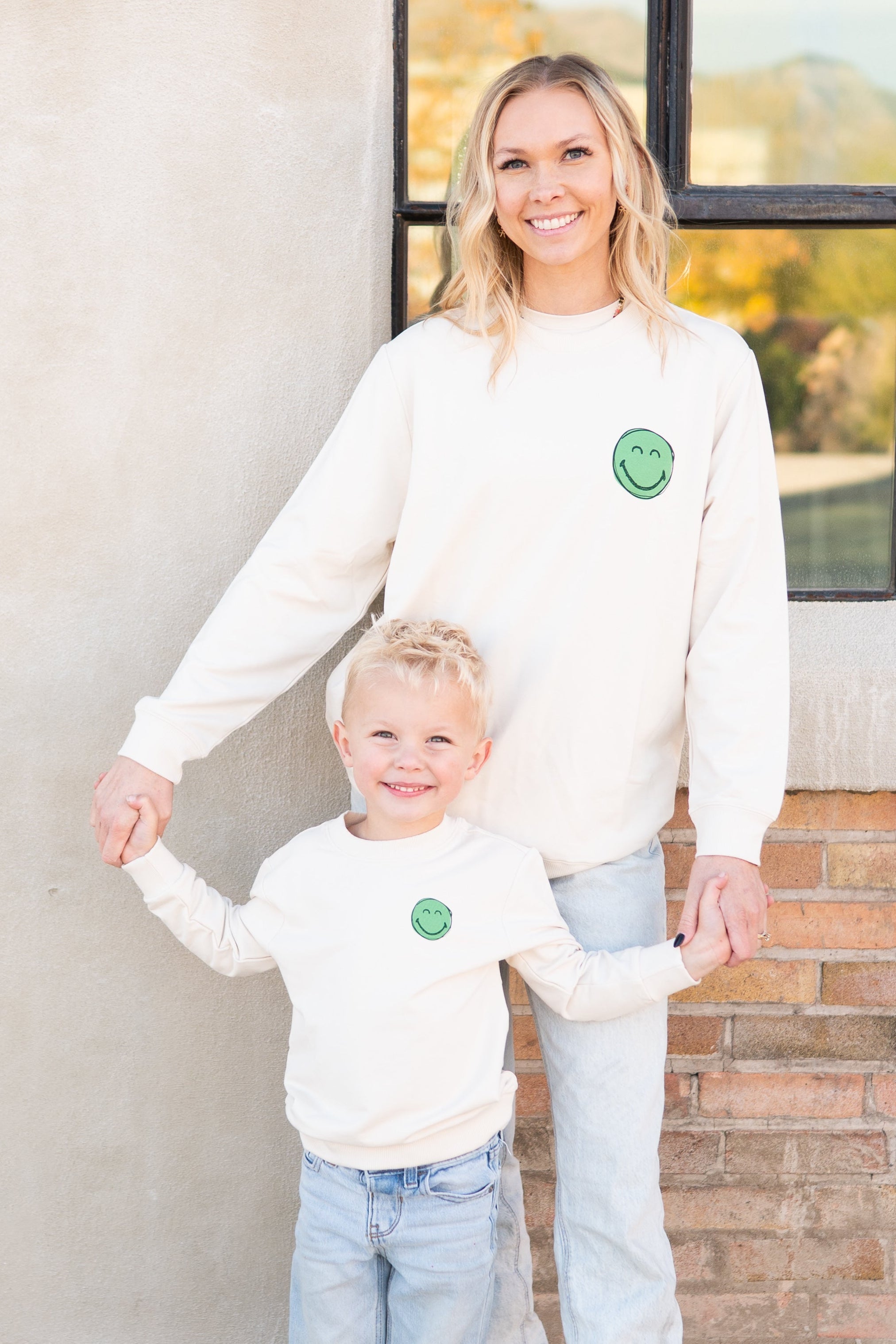 Adult unisex cream crewneck sweatshirt with a green smiley face graphic.