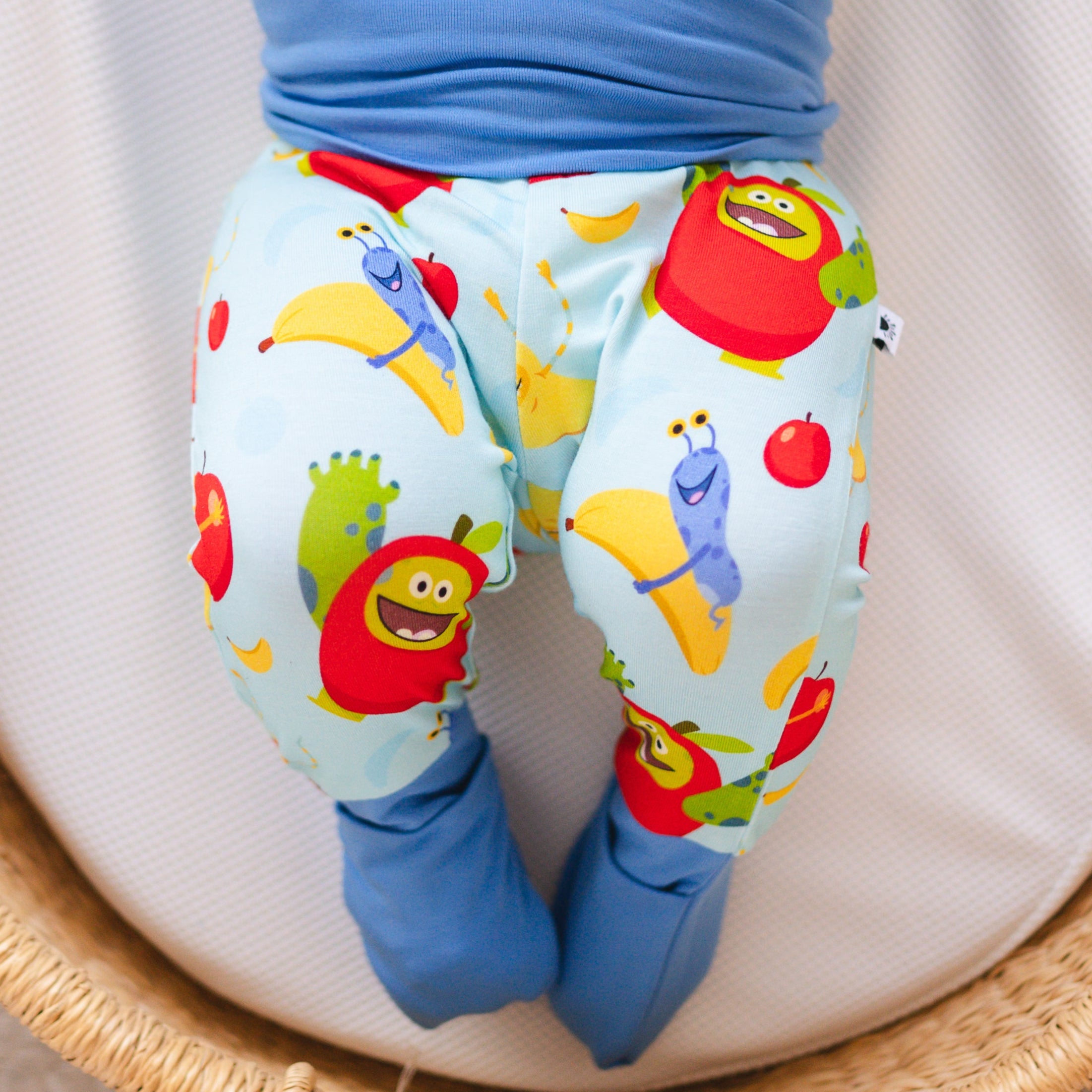 Baby pants with a light blue background and a pattern of cartoon apples and bananas.