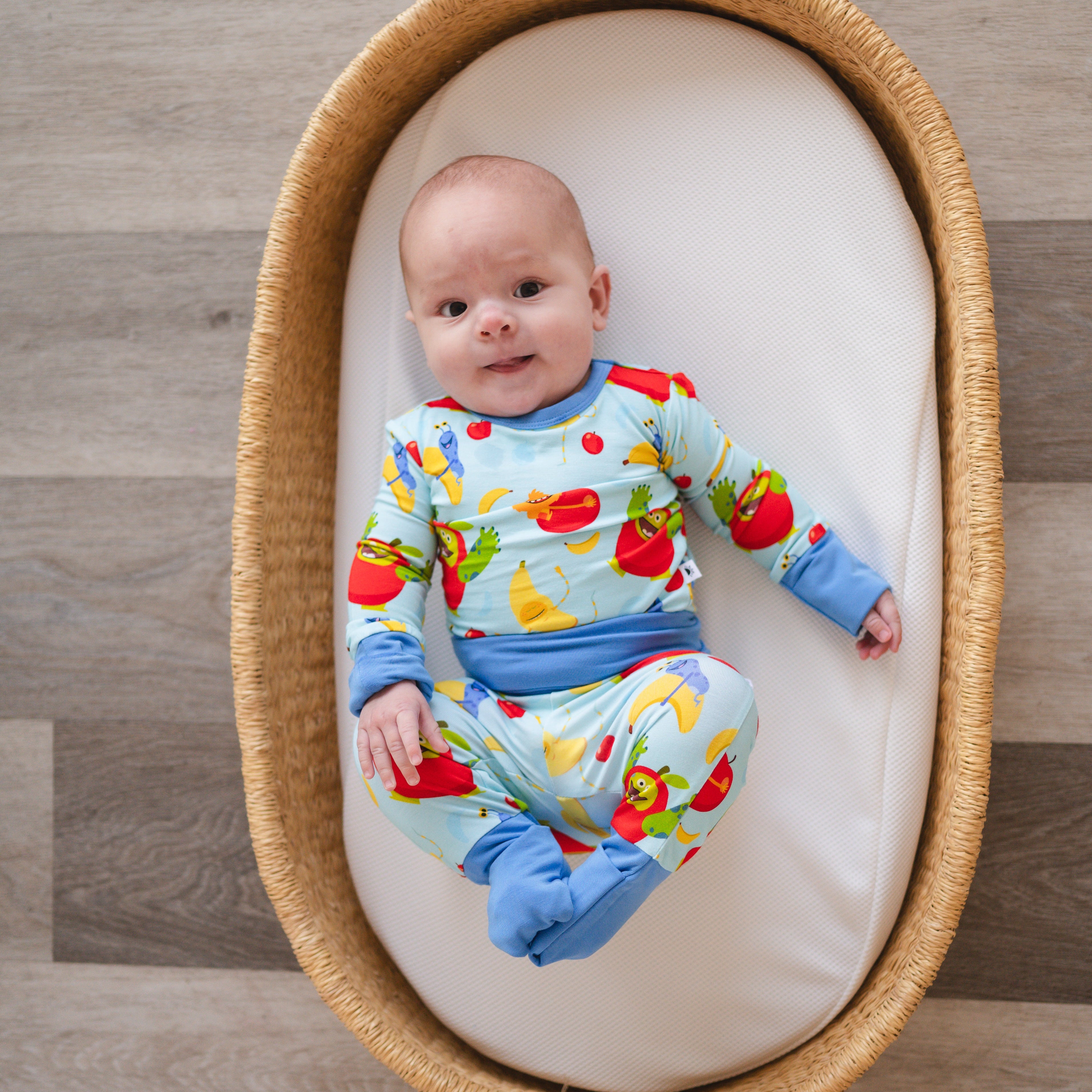 Baby in a light blue pajama set with apples and bananas.