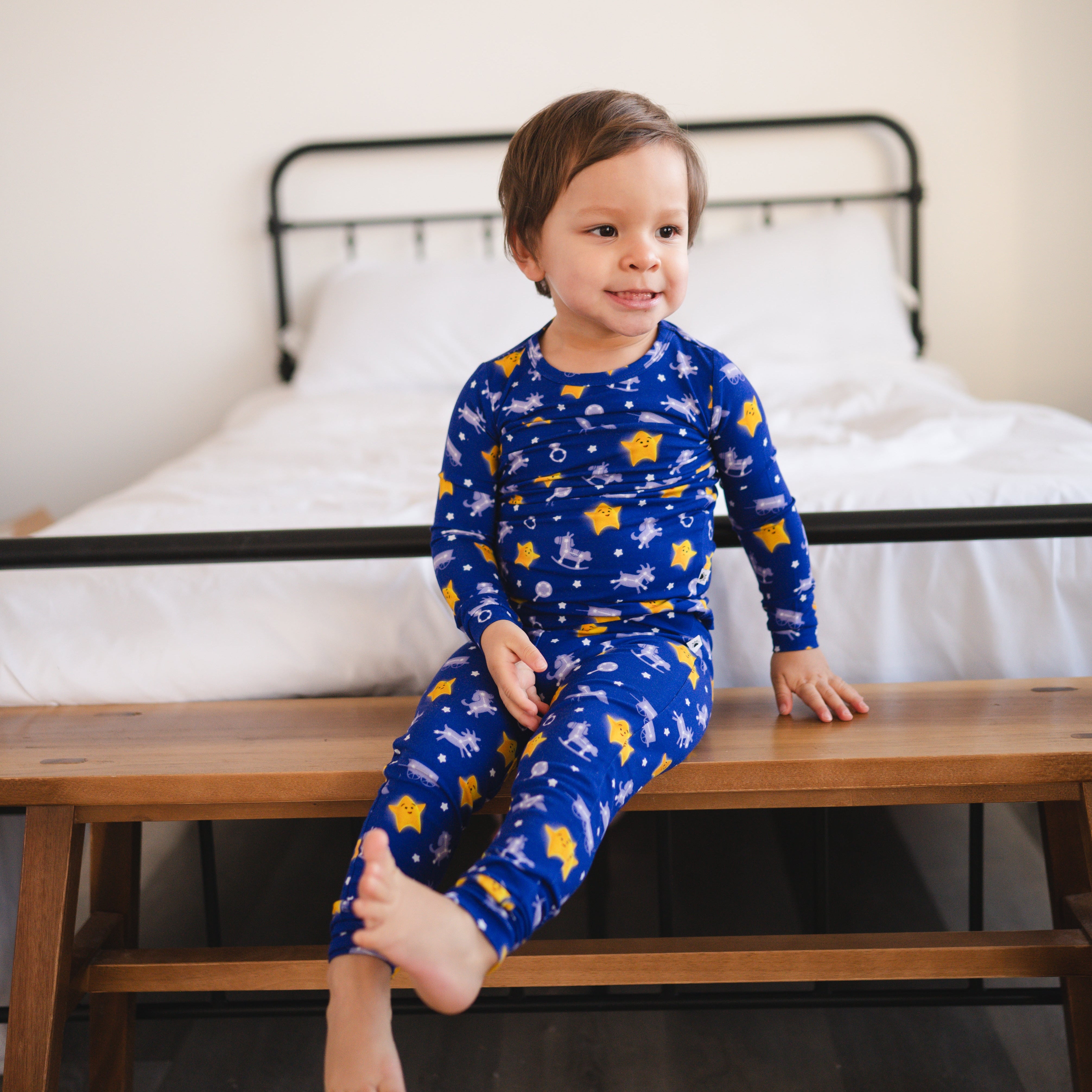 A young child in blue pajamas with yellow stars and rocking horses sits on a wooden bench.