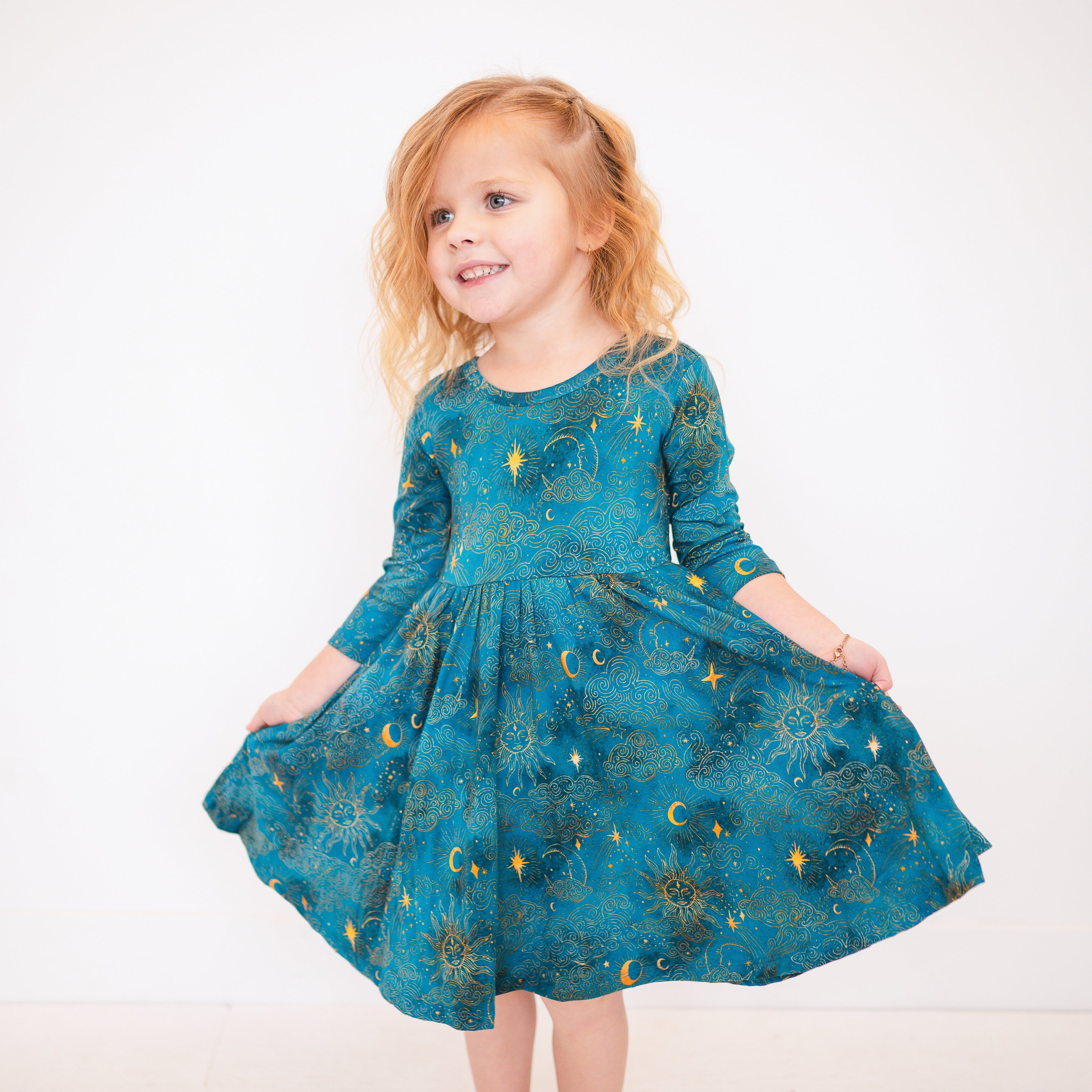 A young girl wears a teal dress with a celestial print of suns, moons, and stars.