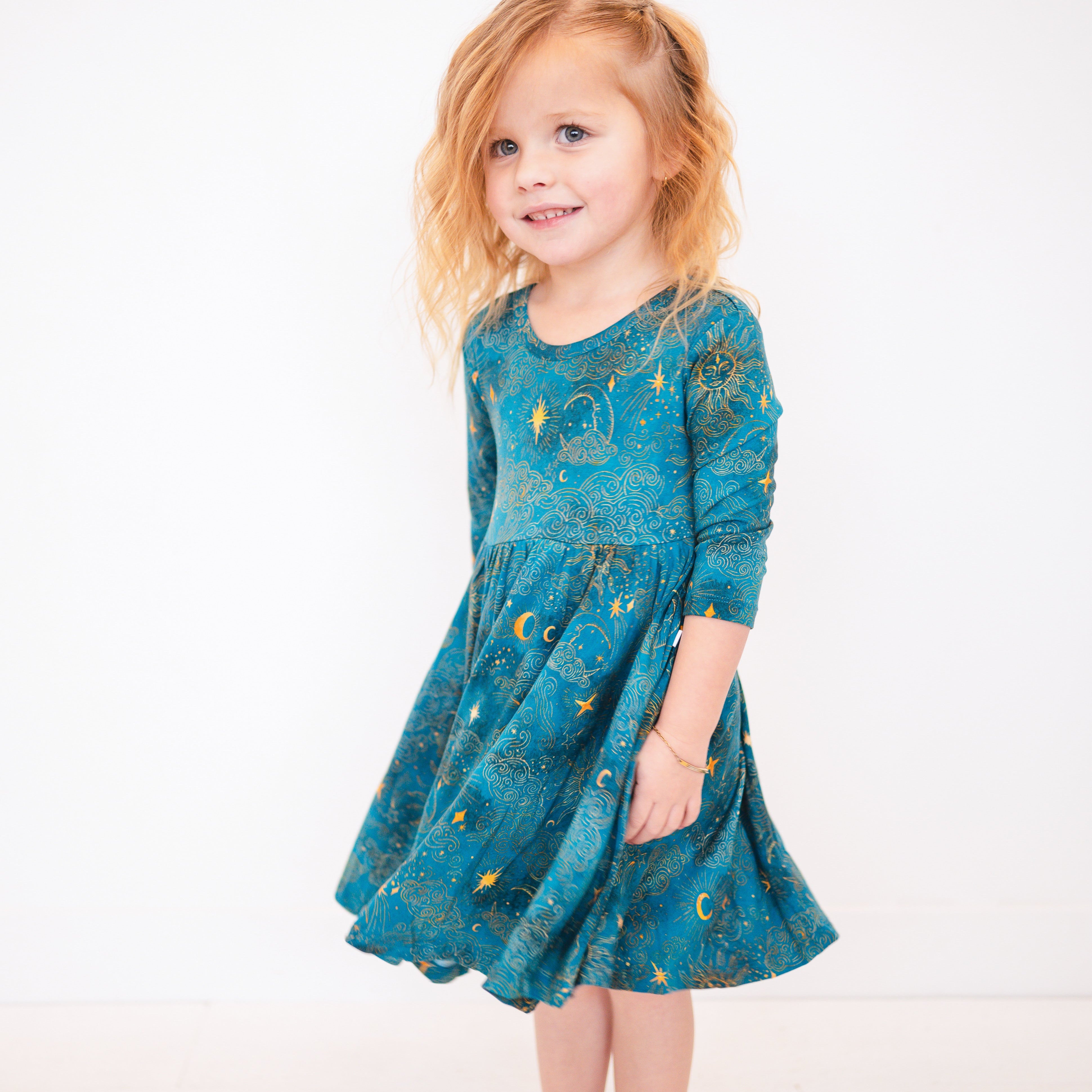 A young girl in a teal dress with a celestial print.