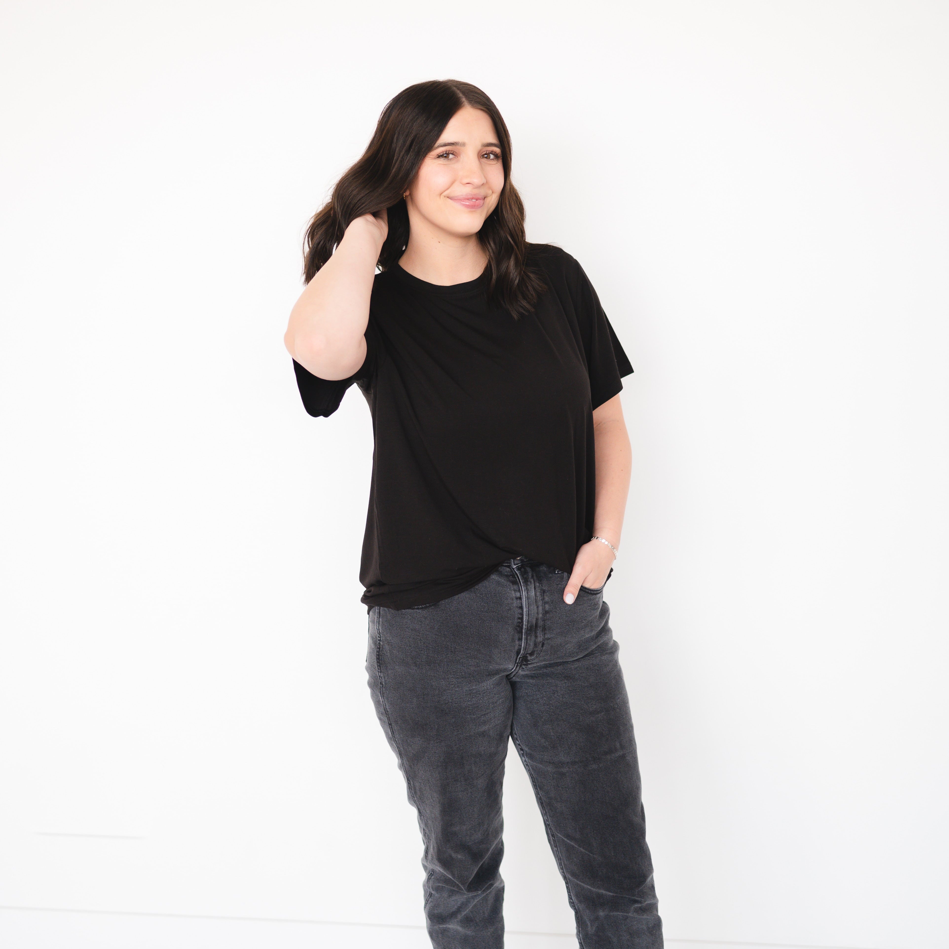 A woman in an oversized black t-shirt and grey jeans poses against a white background.