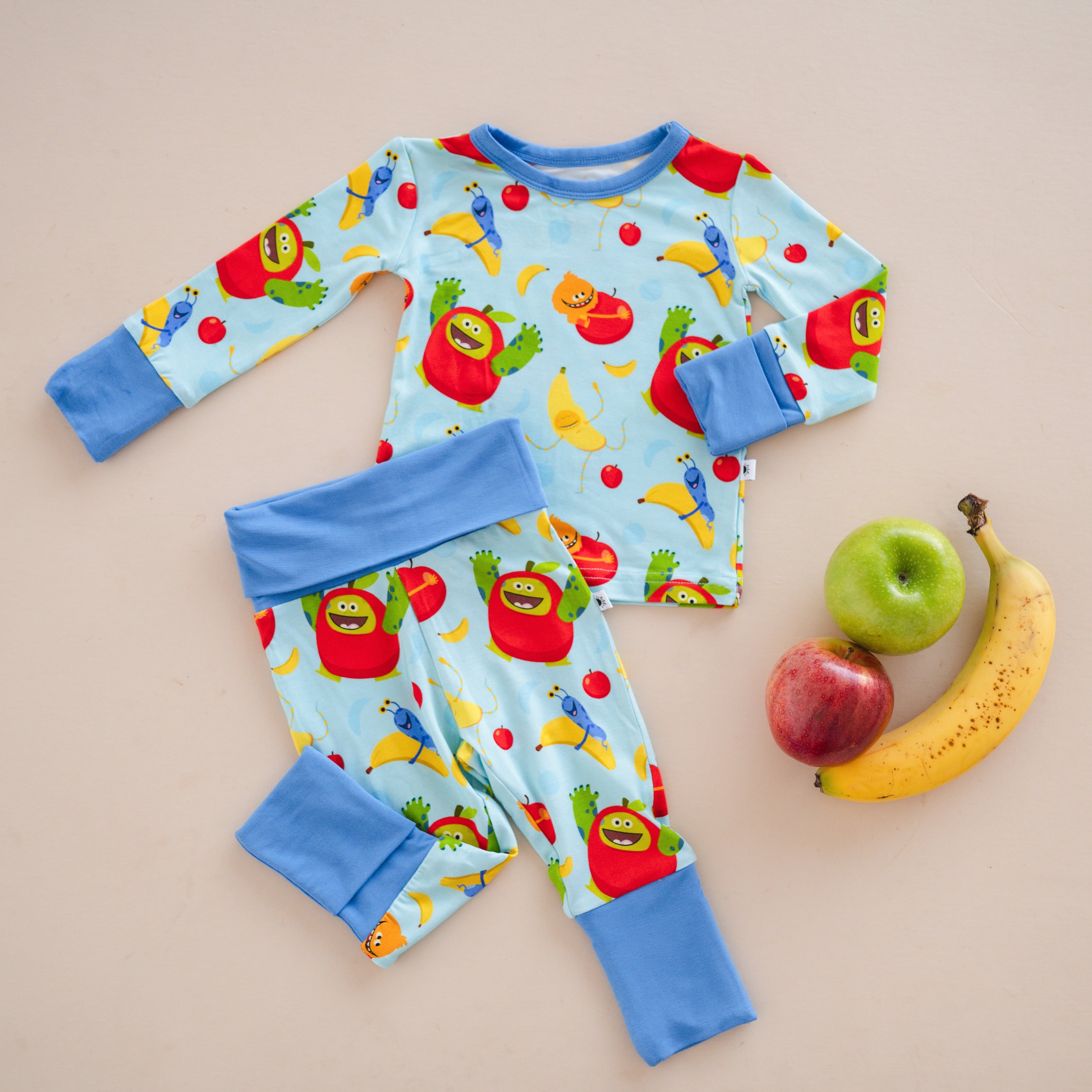 Baby pajamas with apples and bananas print and blue cuffs.