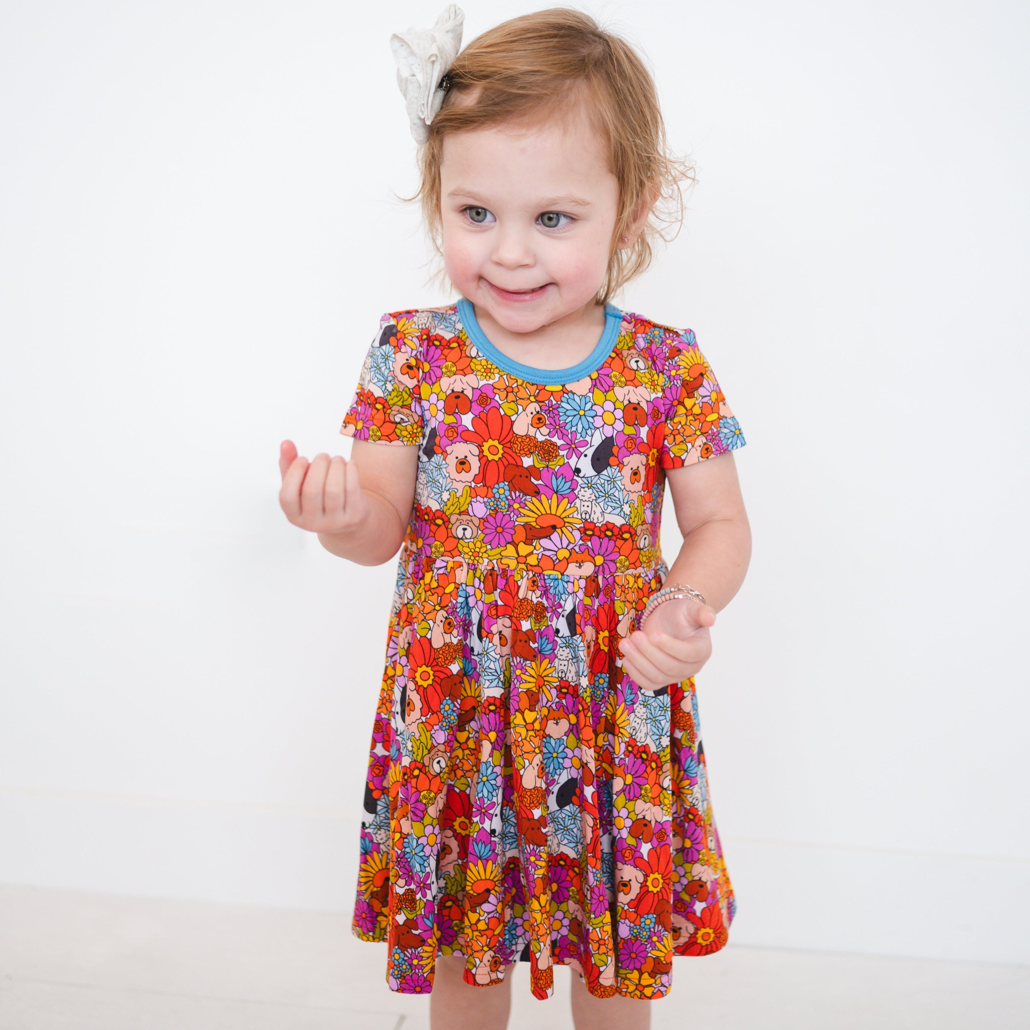 A young girl wears a colorful floral and dog print dress.