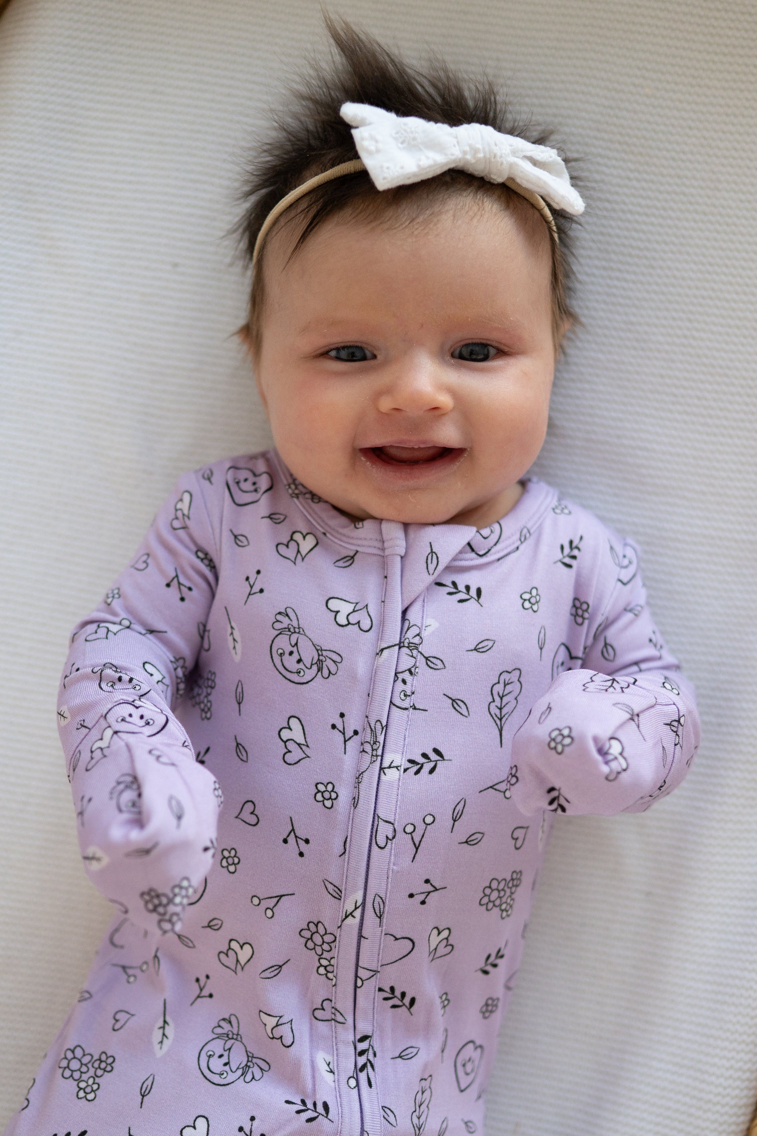 A baby wearing a lilac bamboo pajama set with a doodle print and a white bow.