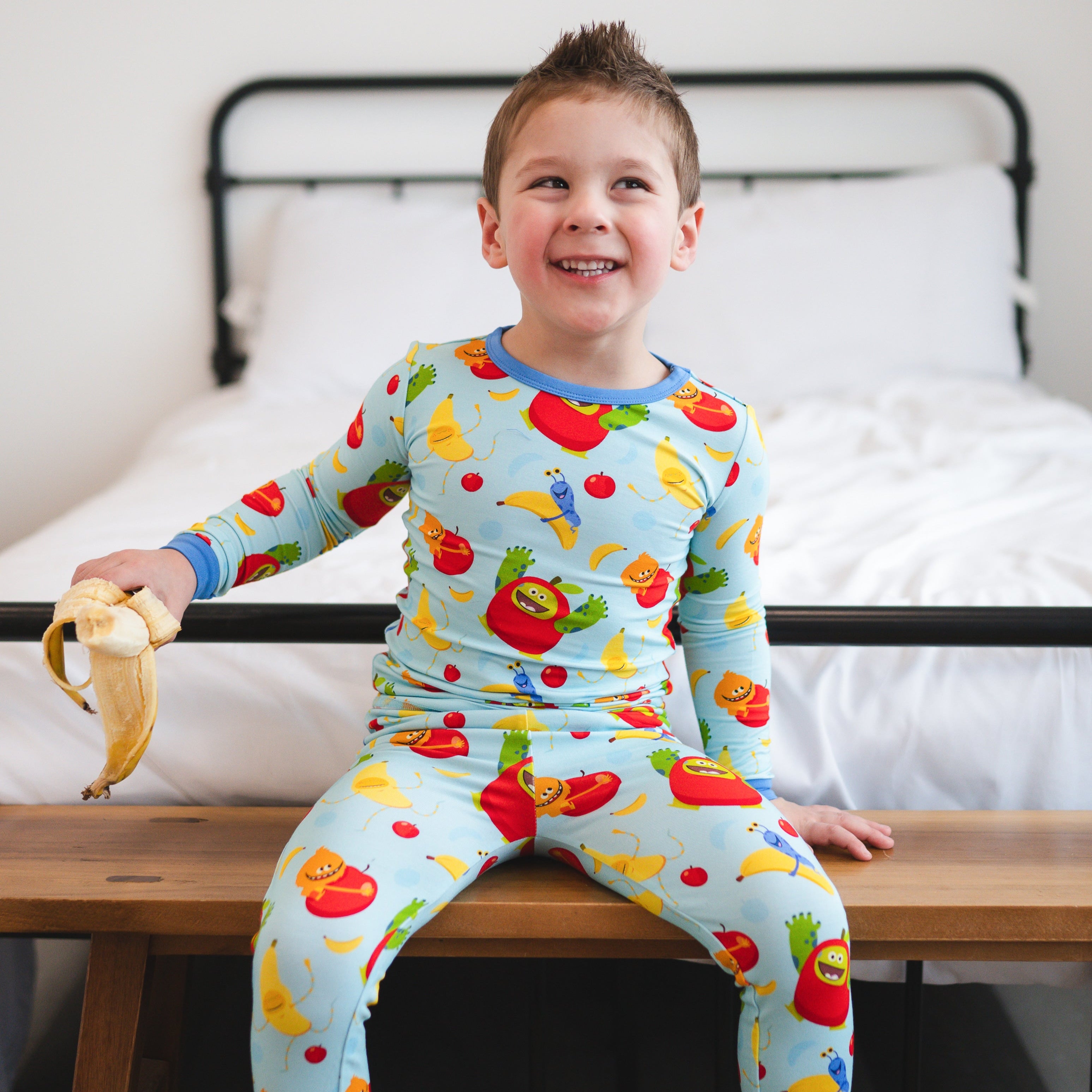 A young boy in light blue pajamas with apples and bananas.