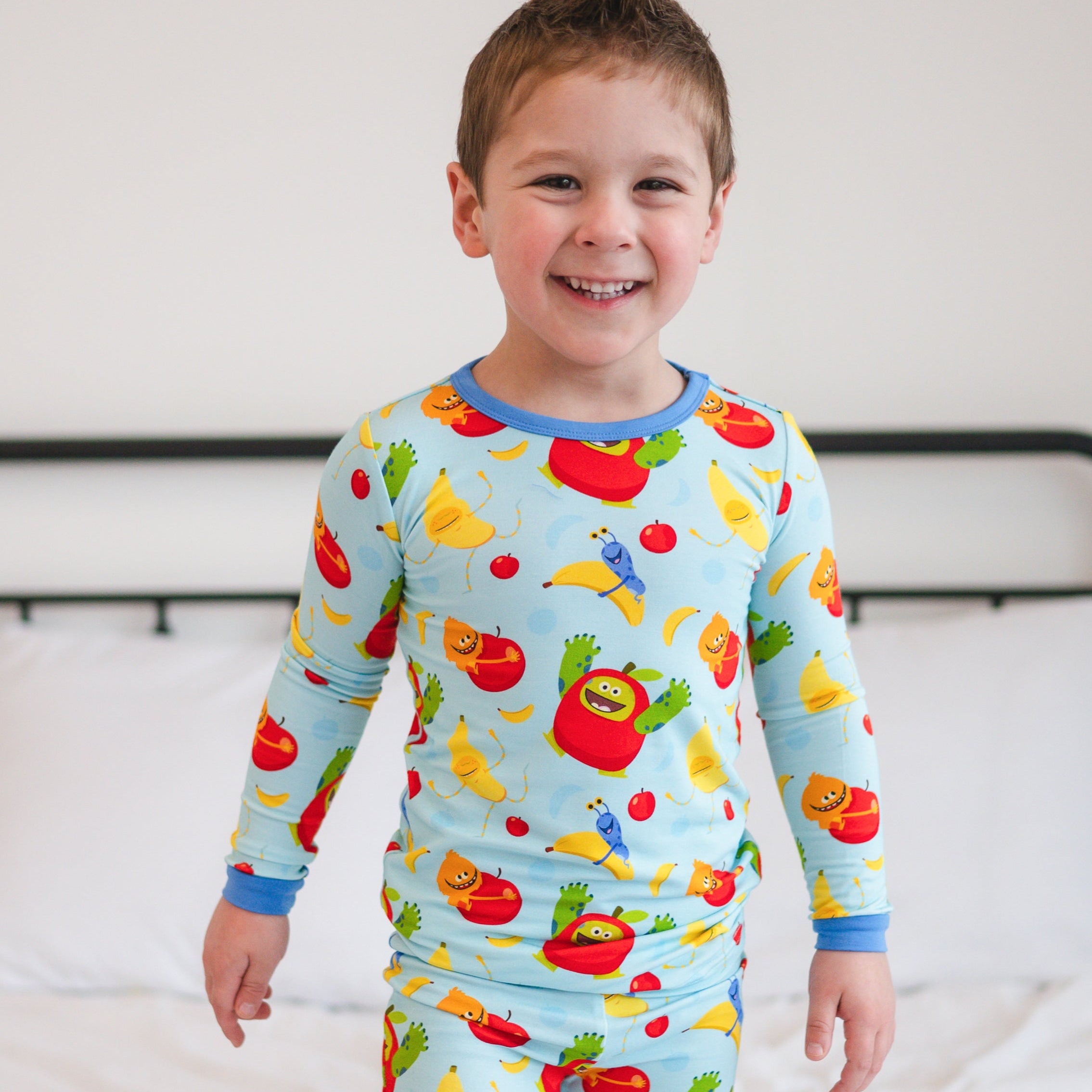 A young boy smiles wearing light blue pajamas with a fruit monster print.