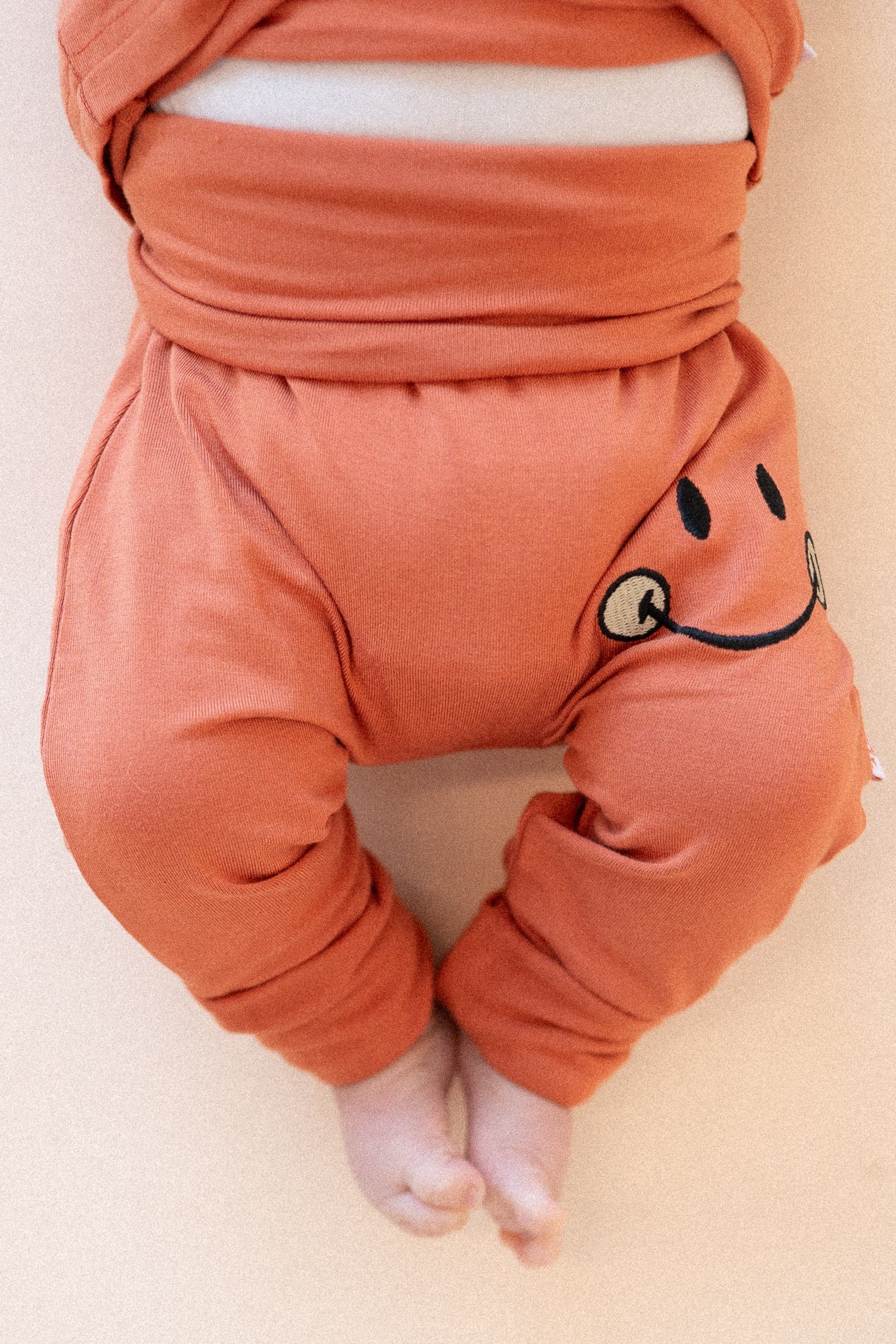 Orange bamboo baby pants with a smiley face detail.