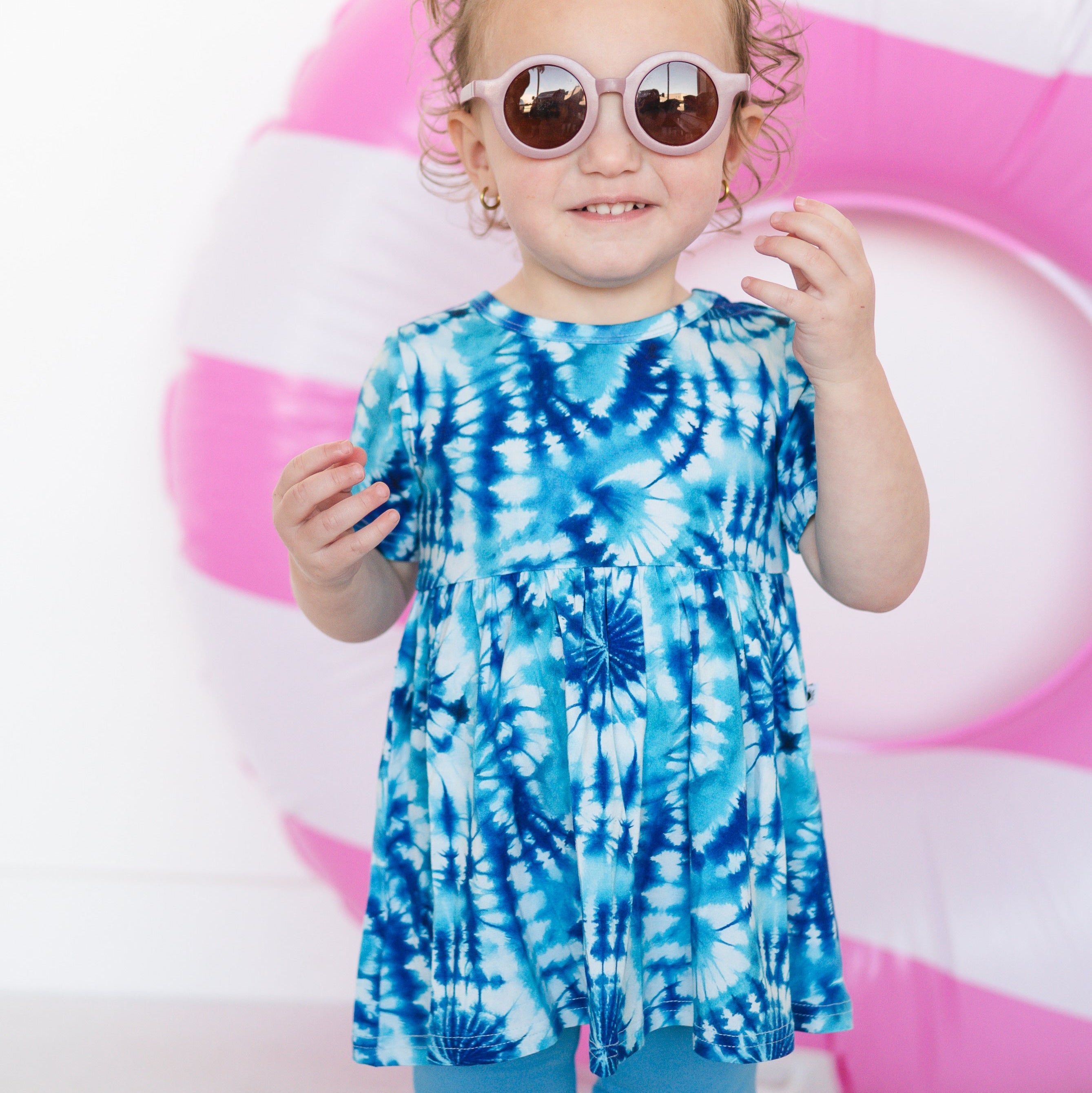 A young girl wears a blue tie-dye peplum top and pink sunglasses.