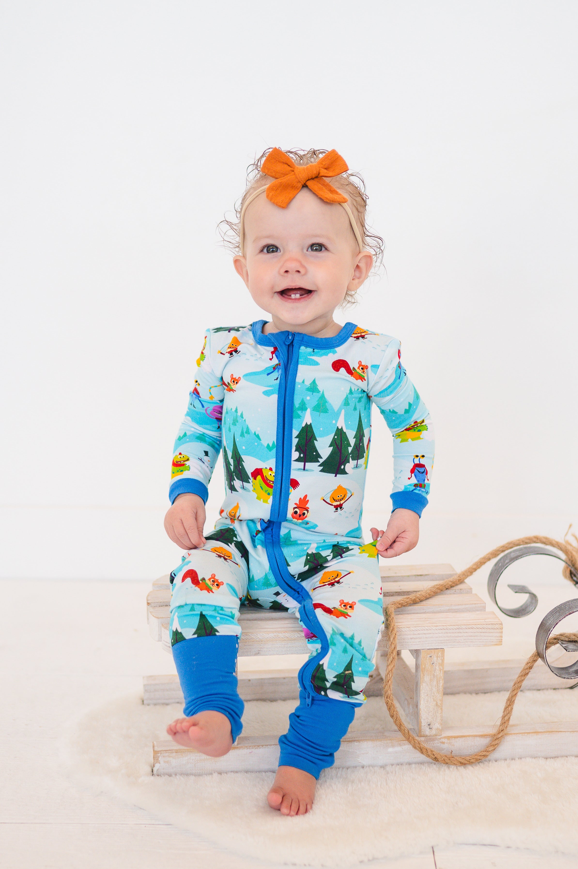 Baby in a blue bamboo zip-up pajama set with a winter forest and character print.