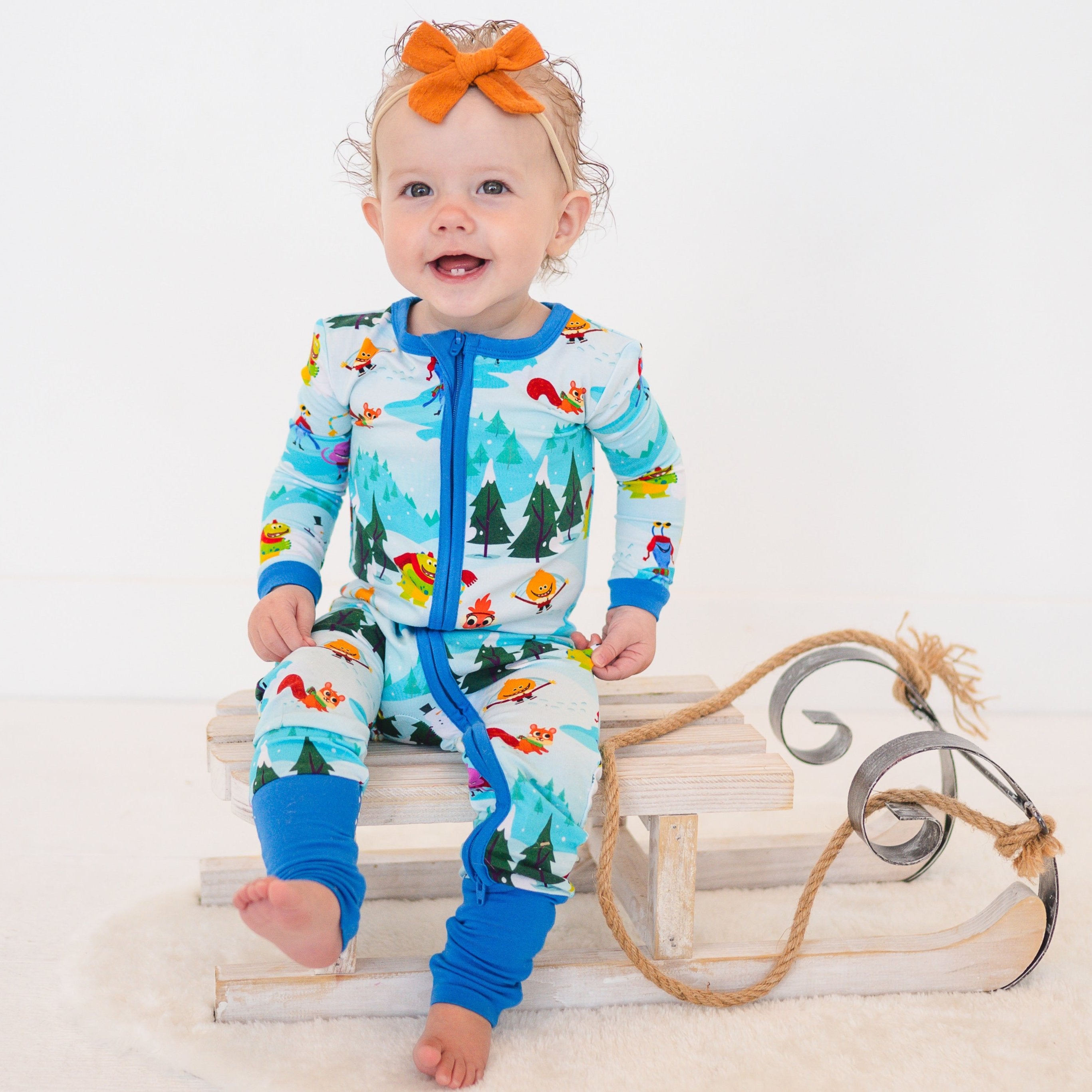 Baby in a light blue bamboo zip-up pajama set with a winter forest and character print.