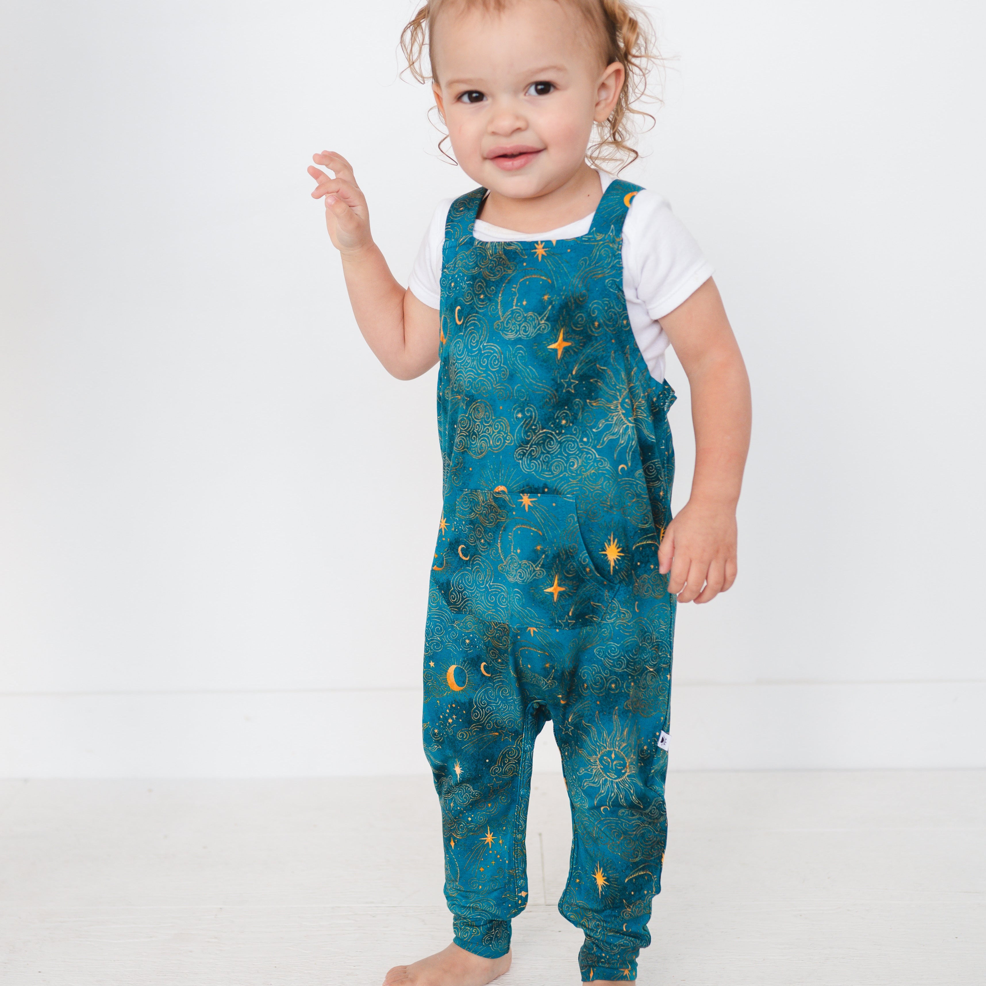 Toddler girl in teal overalls with a celestial print.
